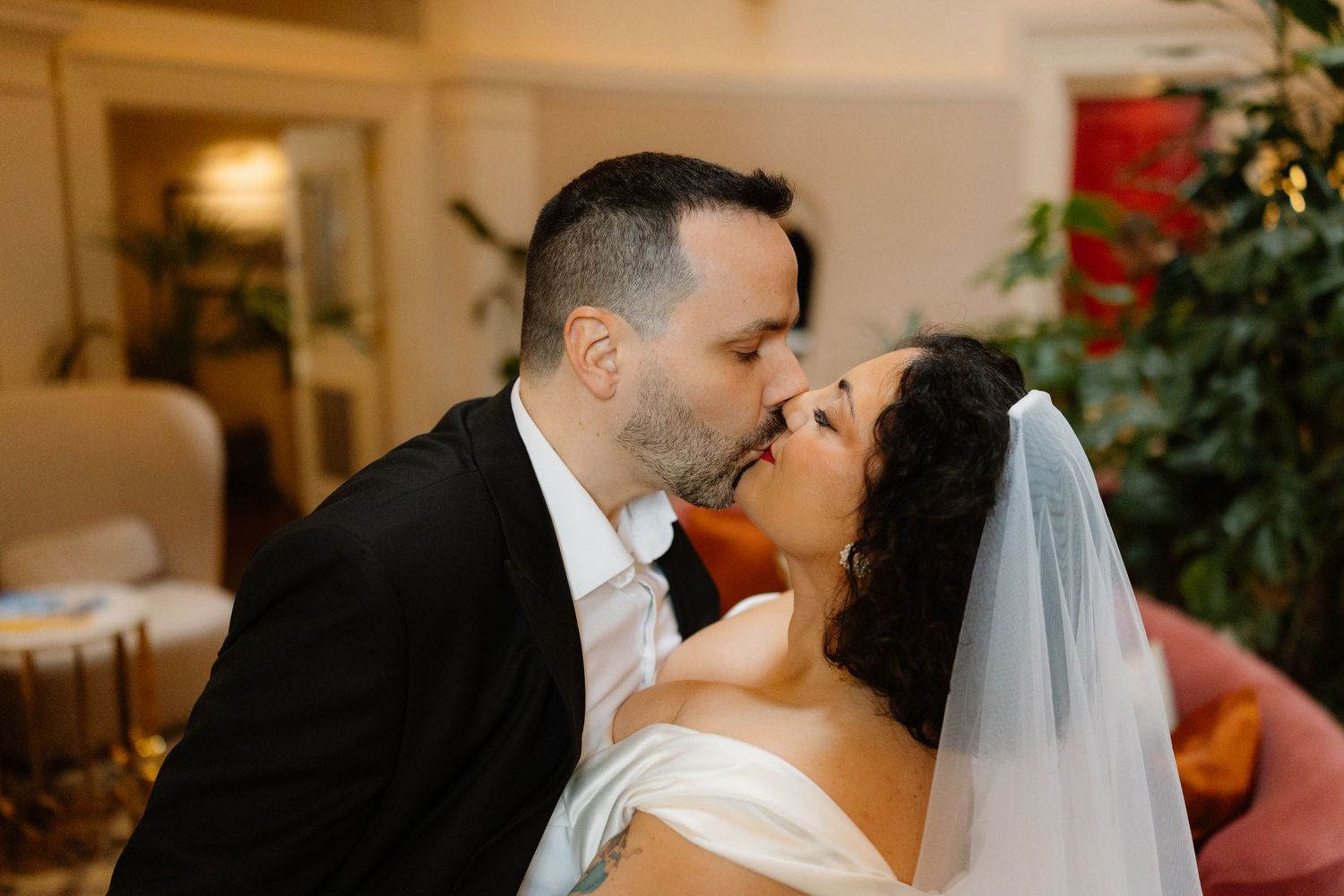 Groom in black suit kisses bride wearing white dress and veil in a tender wedding moment.