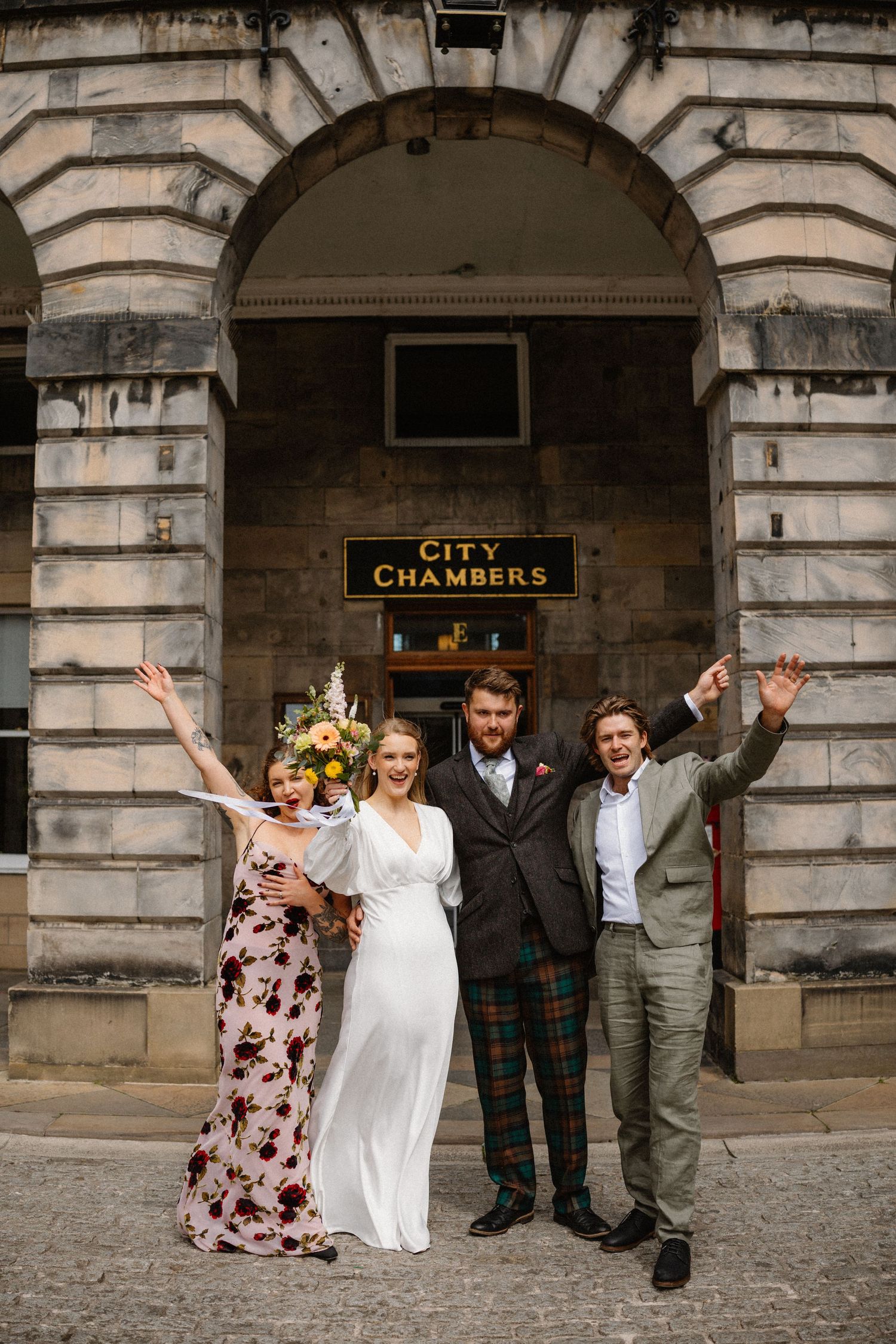 Bride and groom celebrate with two guests outside Edinburgh City Chambers on their wedding day.
