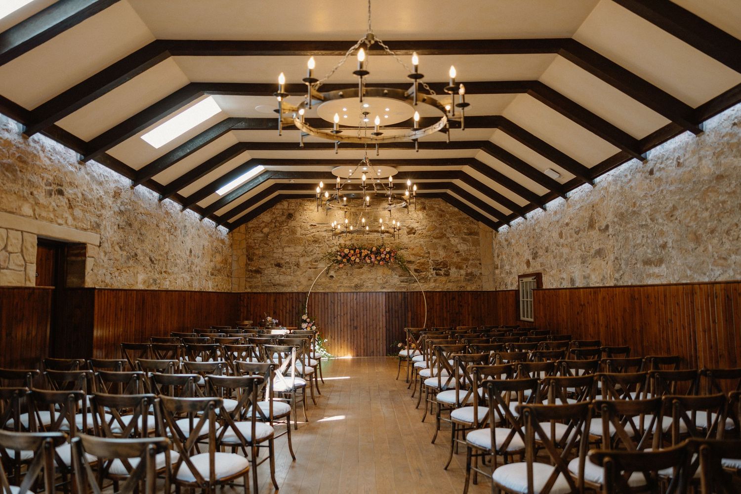 Rustic wedding ceremony venue with exposed wooden beams and rows of chairs set up in a barn-like interior.