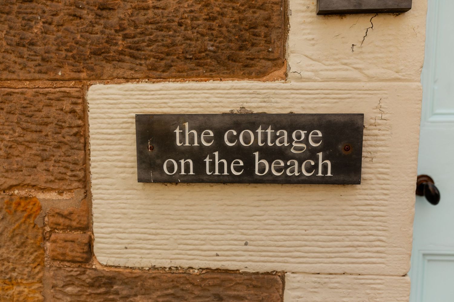 Wooden signs with text mounted on a cream-colored wall display cottage-themed messages.