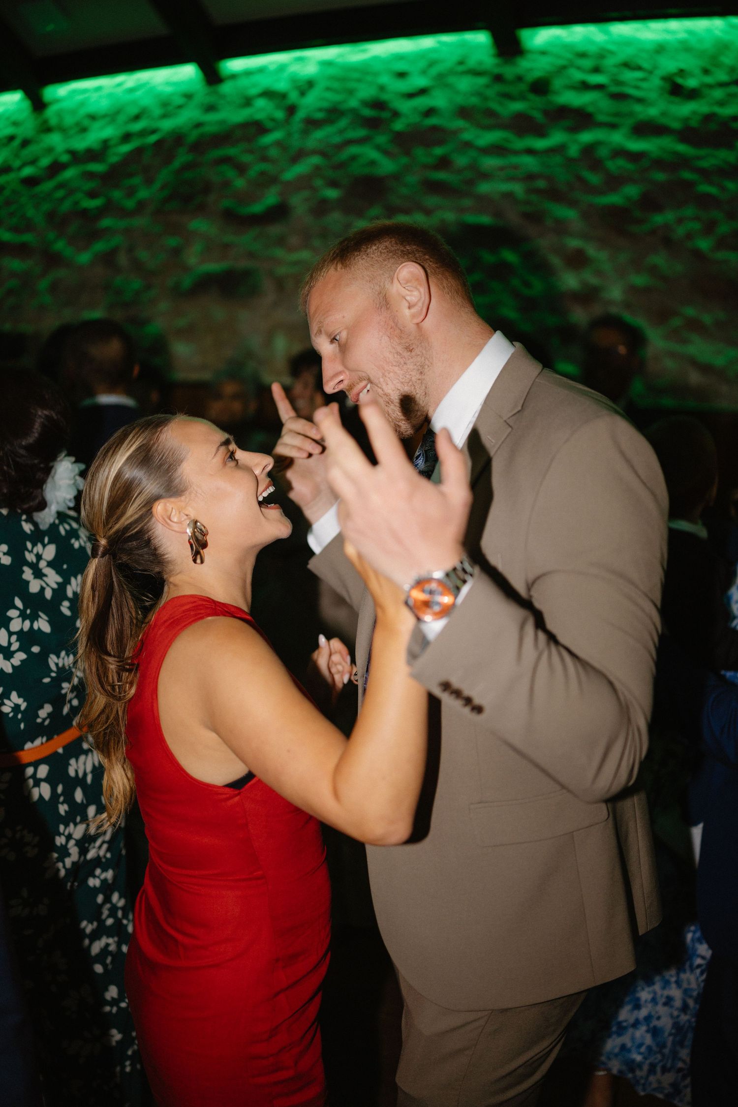 Couple dancing energetically under green lighting at a reception party.