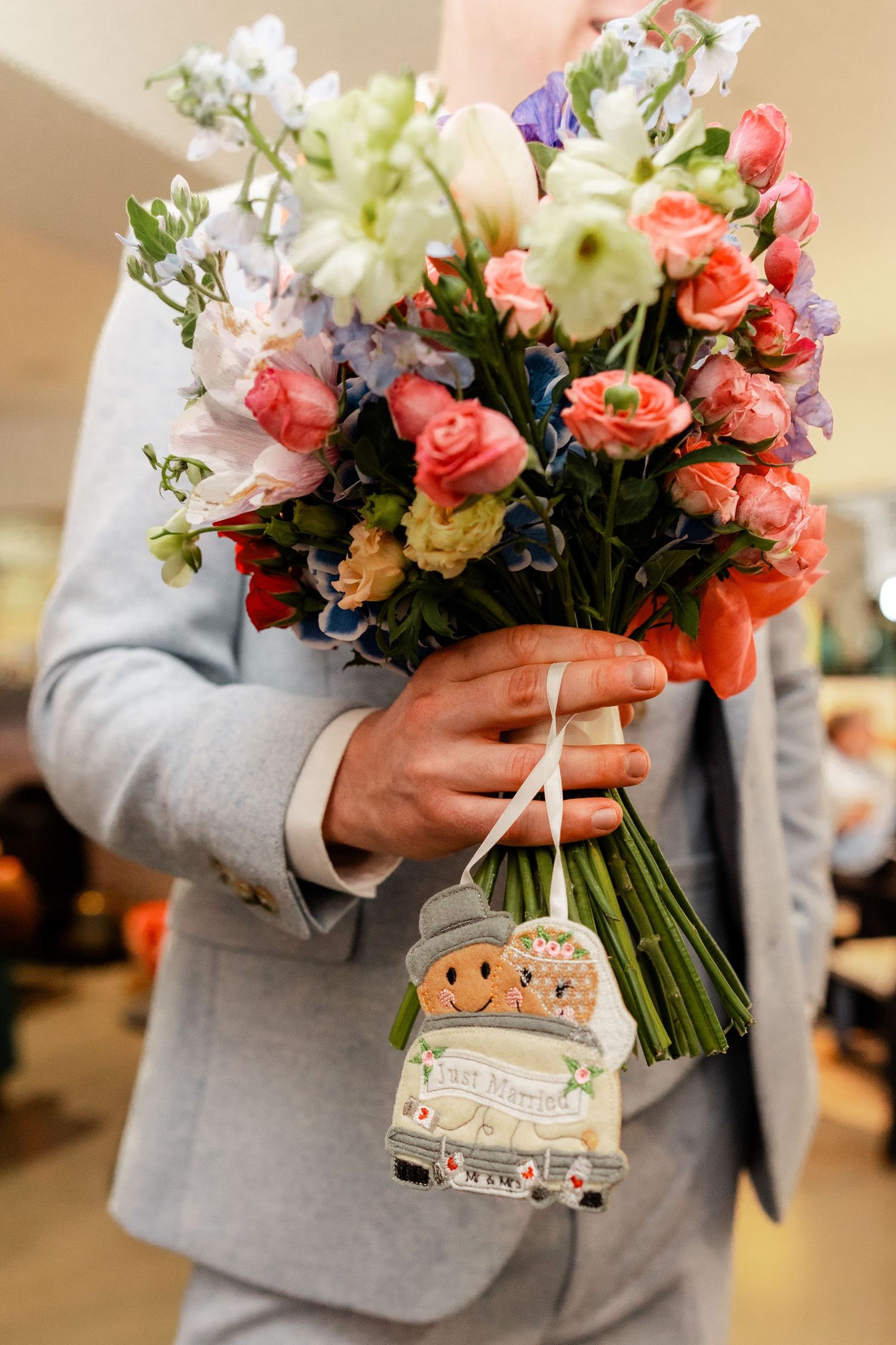 A bouquet of coral roses and white flowers held by someone wearing a light gray suit jacket.