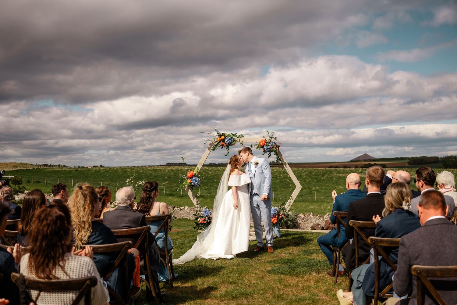 Panoramic view of an outdoor wedding ceremony against a dramatic landscape with cloudy skies.
