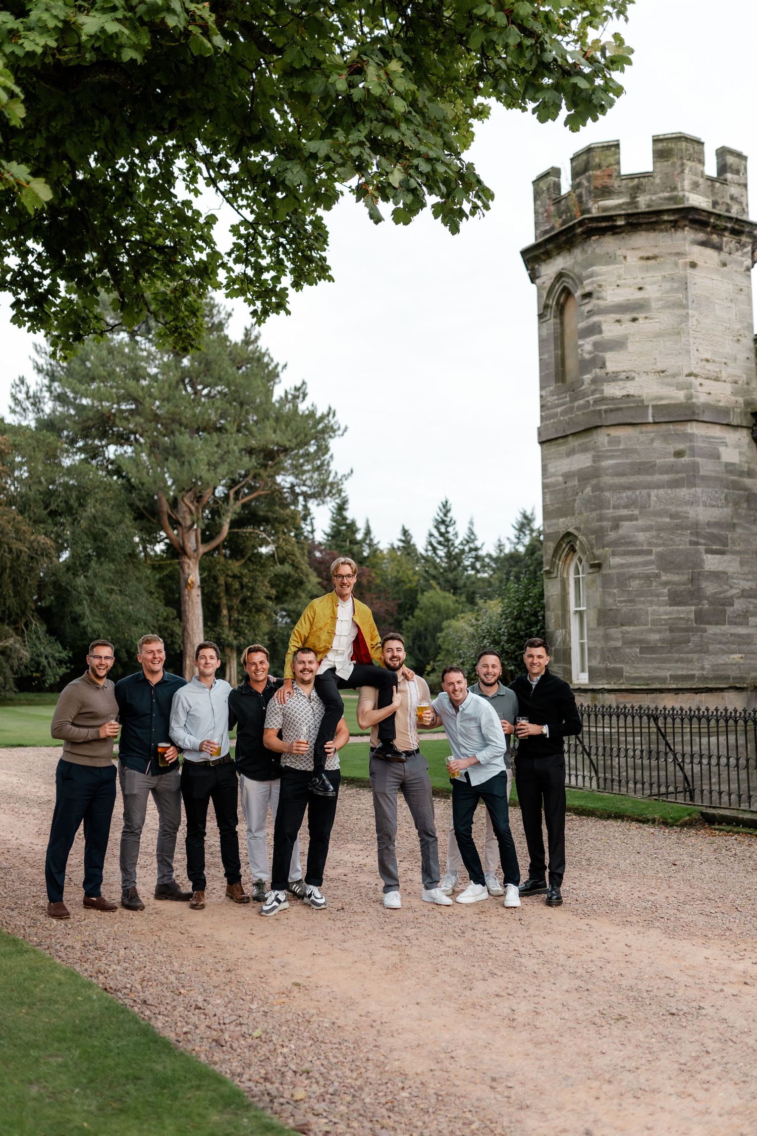 A group poses together on a path near a stone castle tower surrounded by trees.