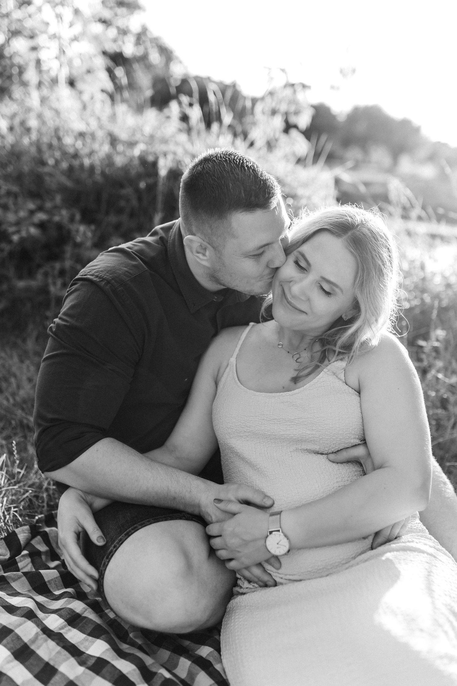 Romantic black and white maternity photos showing intimate couple poses on a blanket outdoors.