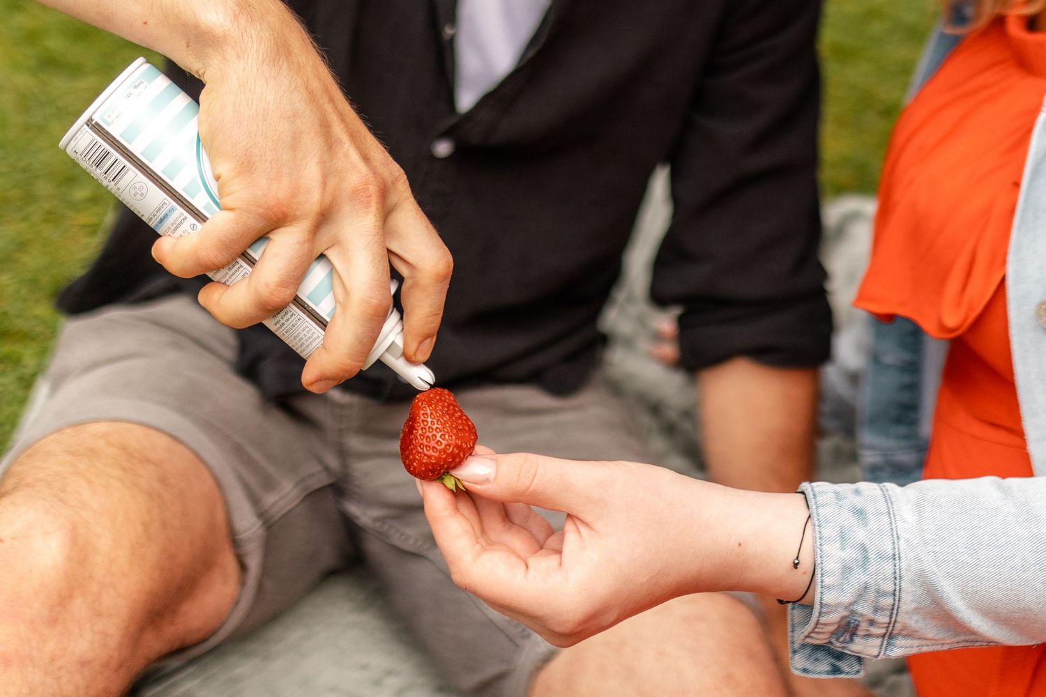 Couple sharing strawberries during romantic outdoor picnic on grass.