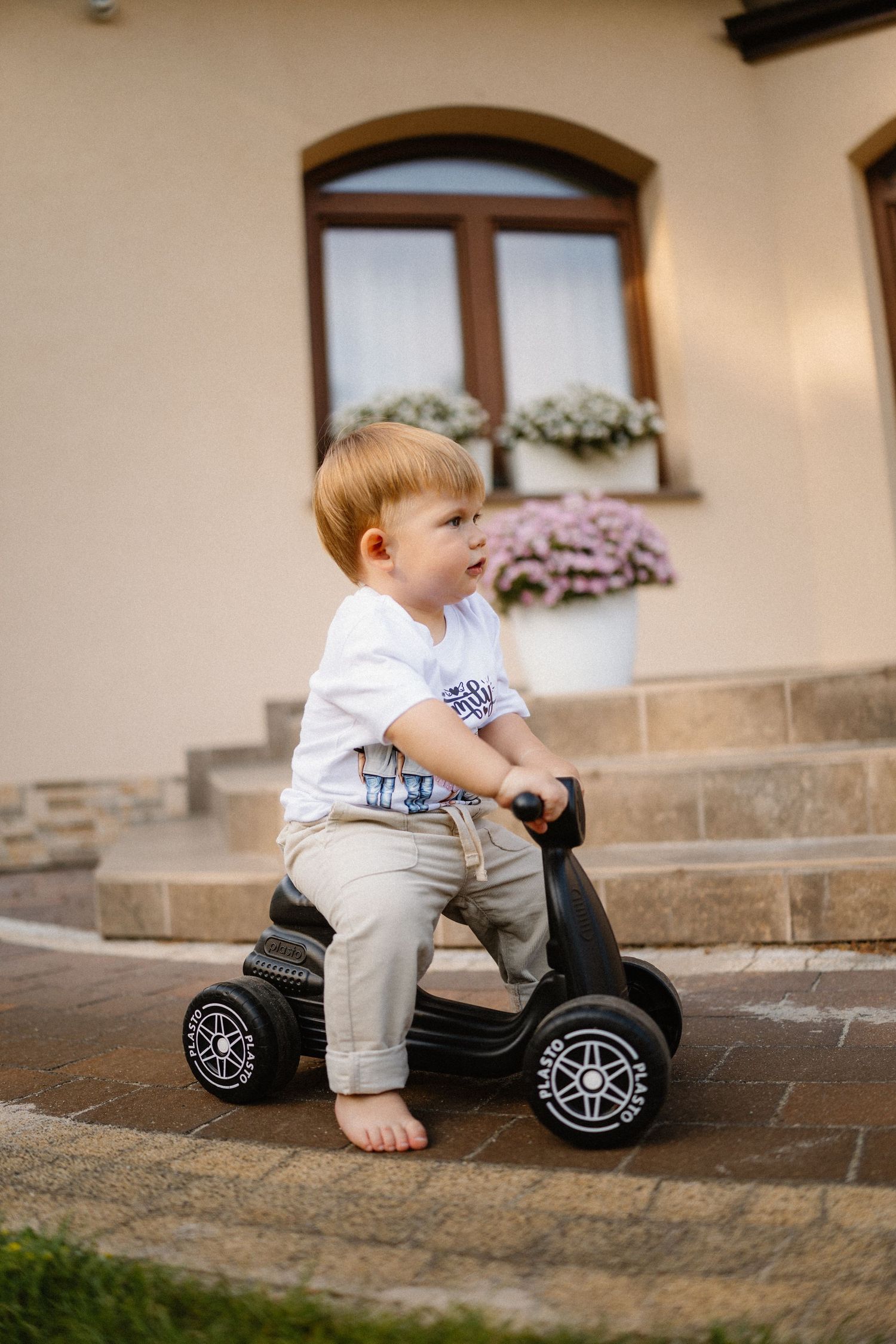 A small child plays with a black toy motorcycle on stone pavers.