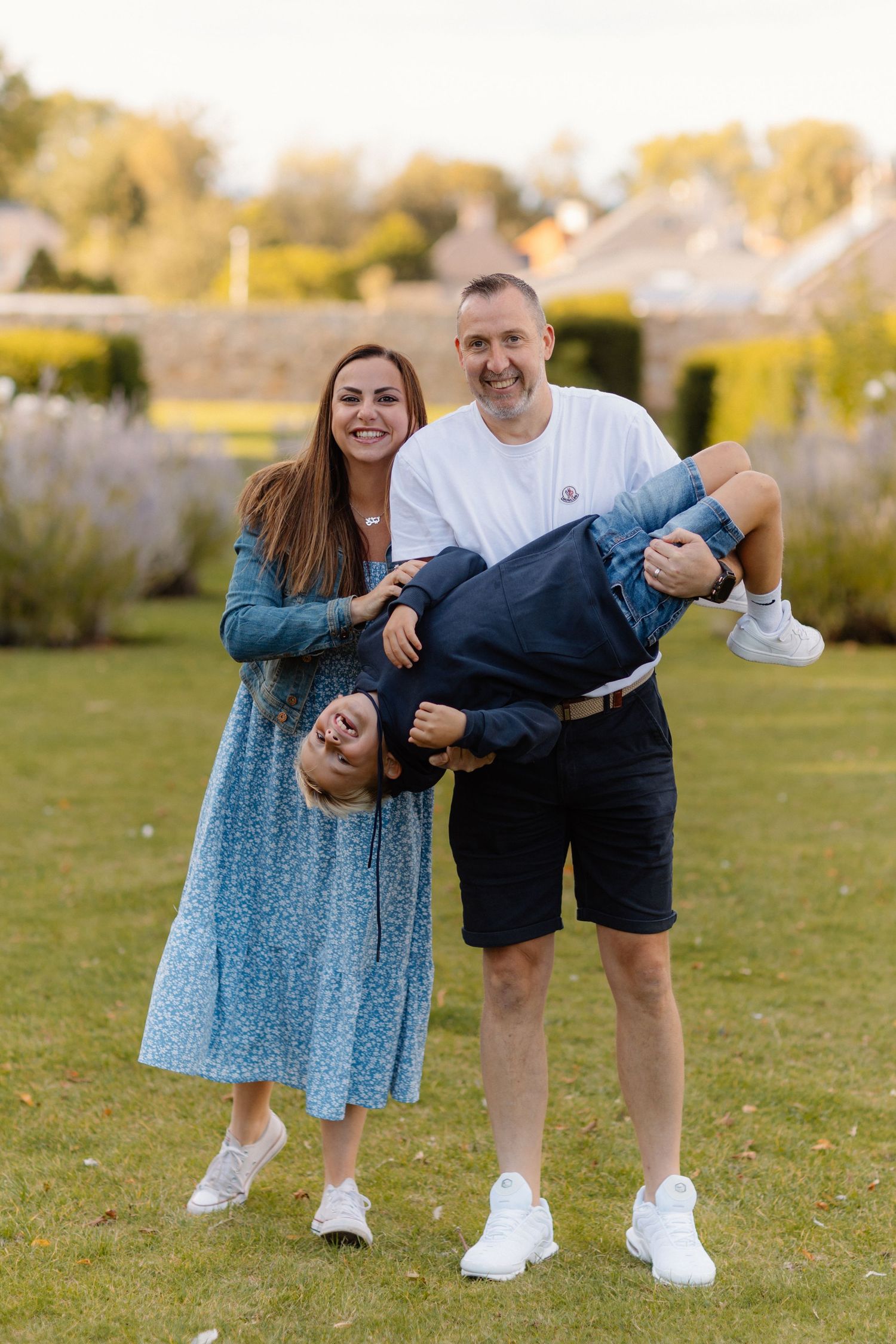 Happy family moment in a garden with parents playfully holding their child upside down.