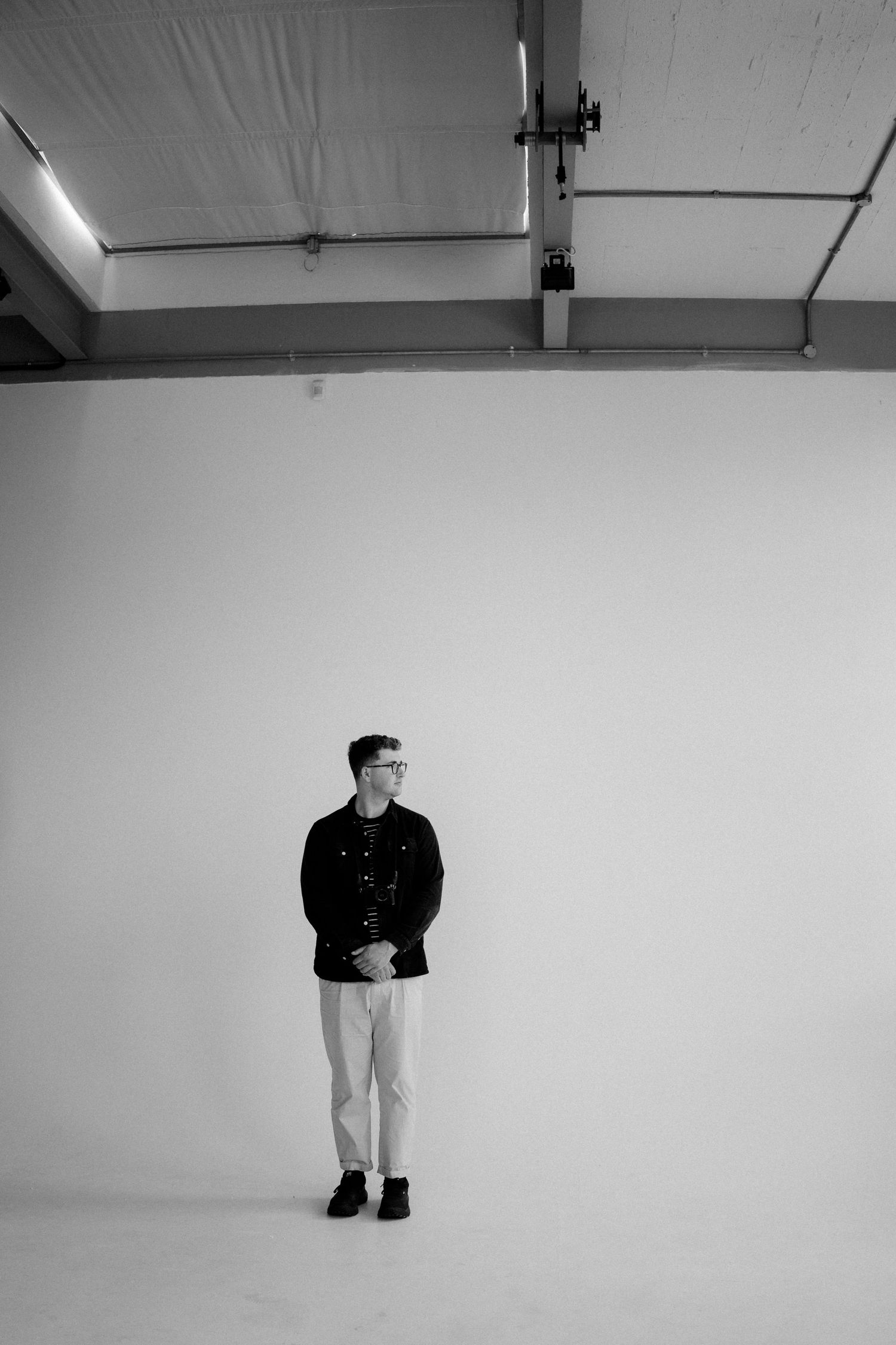 Minimalist black and white photo of person standing against white studio wall.