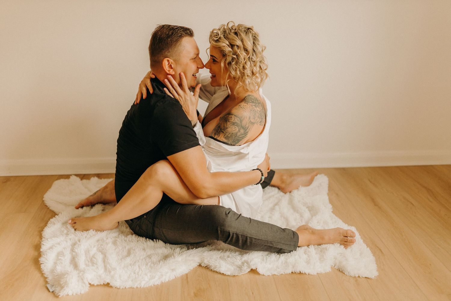 Intimate couple photoshoot on white bedding in a bright indoor setting.