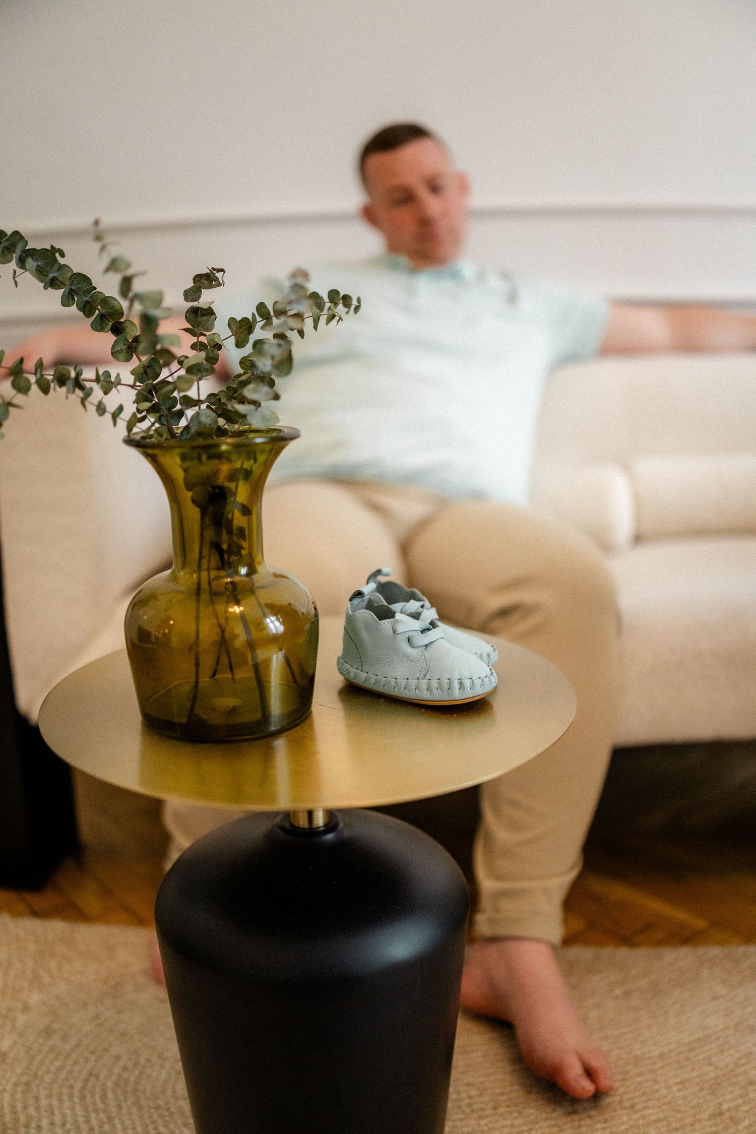 Minimalist living room decor featuring amber glass vase with greenery on round side table.