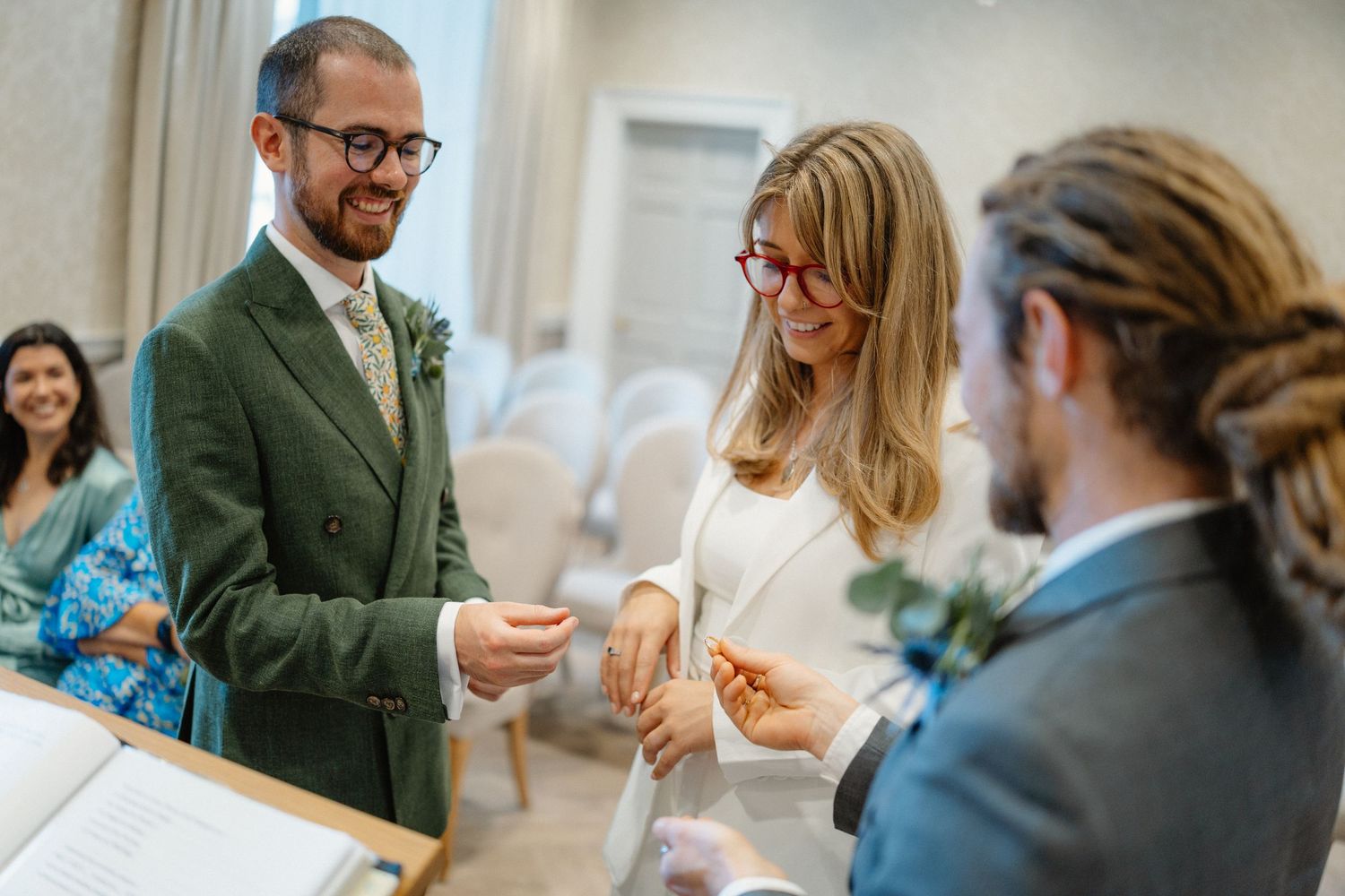 A wedding ceremony takes place indoors as people gather for an intimate exchange of rings.