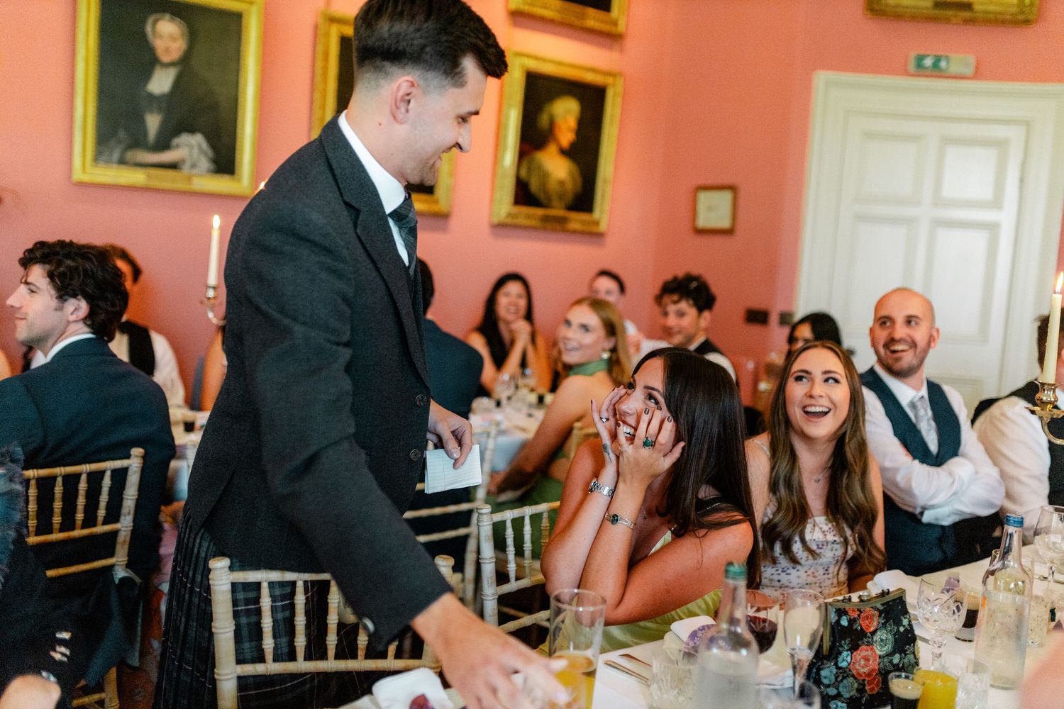 Wedding reception guests laughing and socializing in a formal pink dining room.