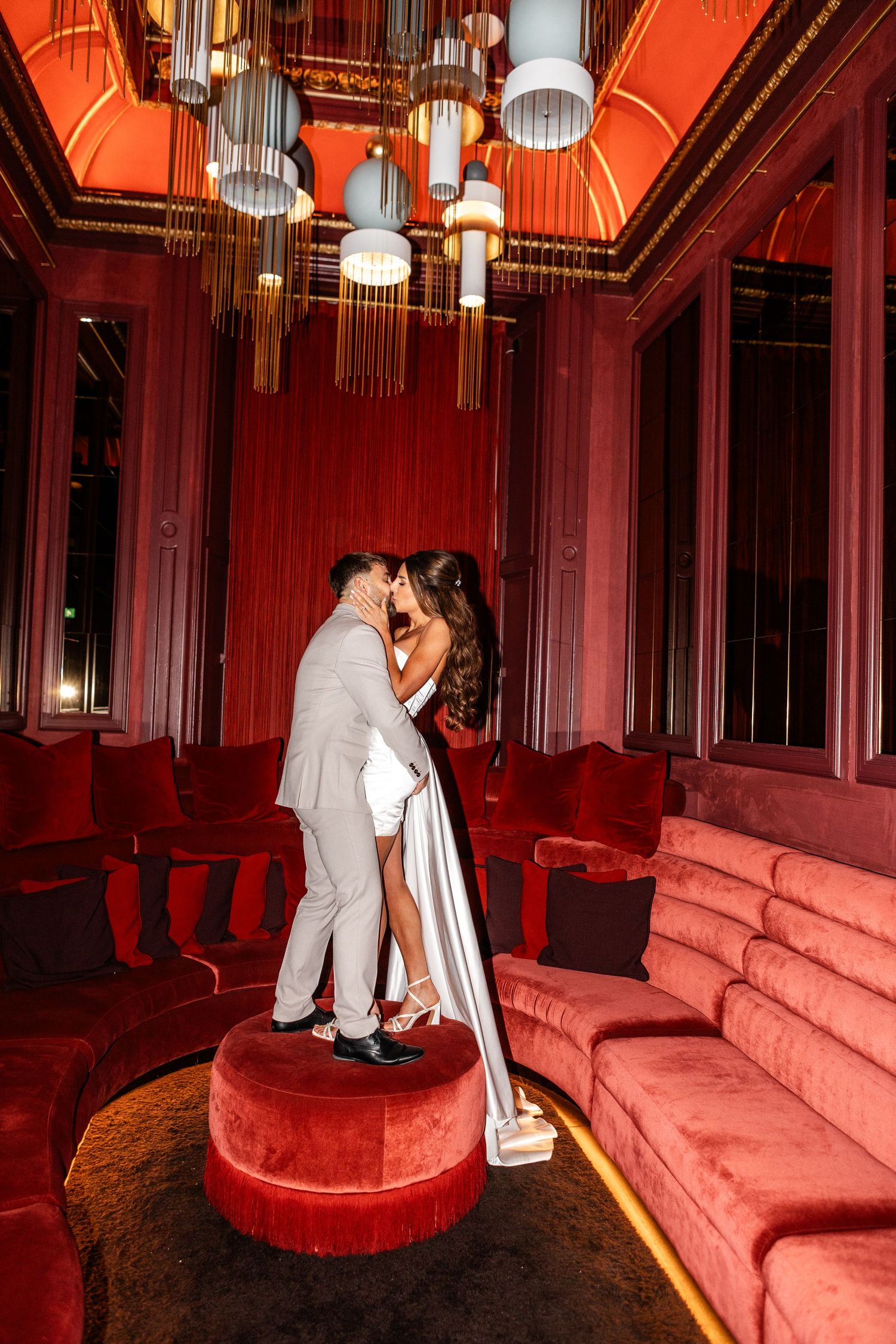 Dramatic red-lit lounge setting captures romantic moments between newlyweds.