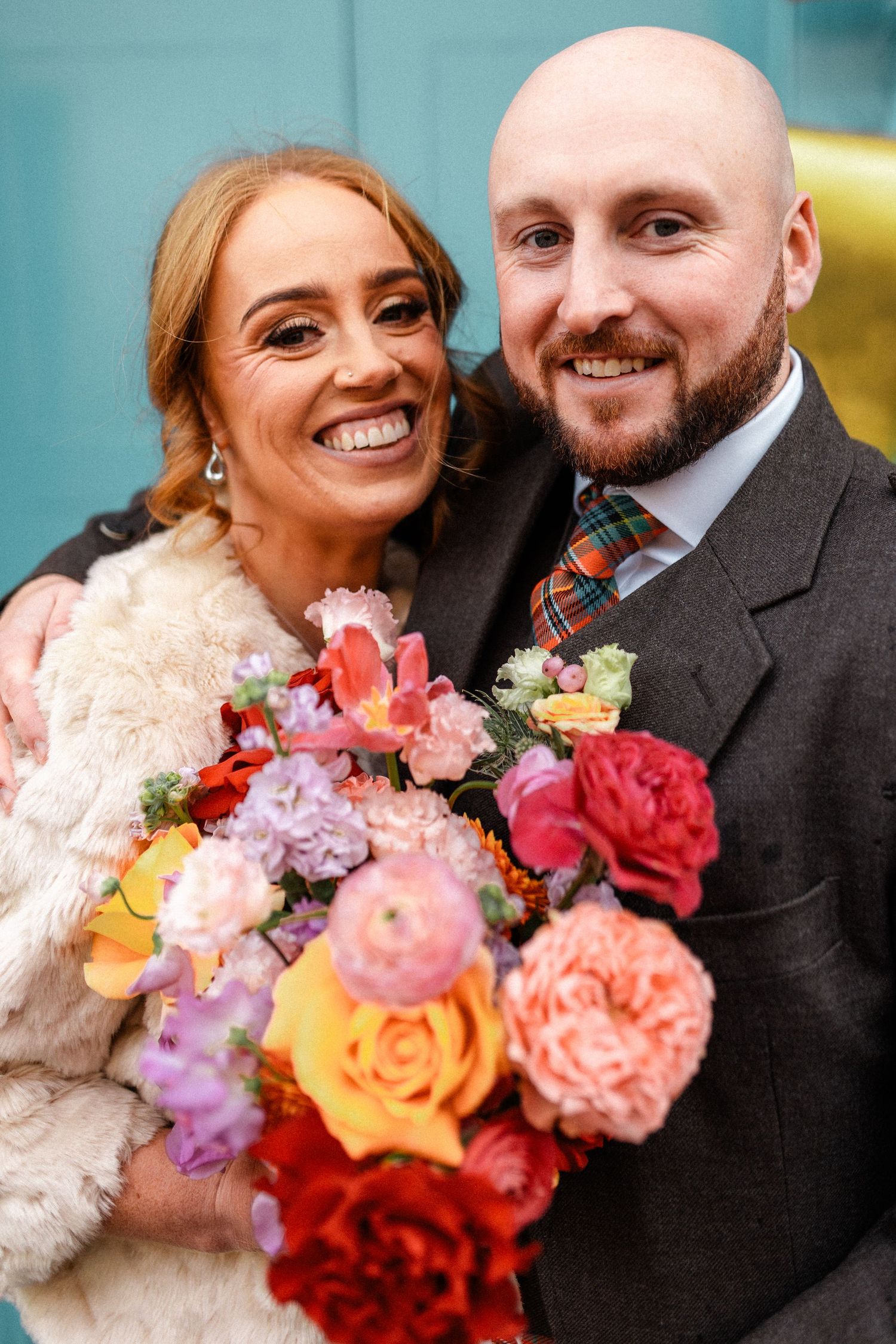 A vibrant bouquet of roses and mixed flowers adds color to a wedding portrait against a blue background.