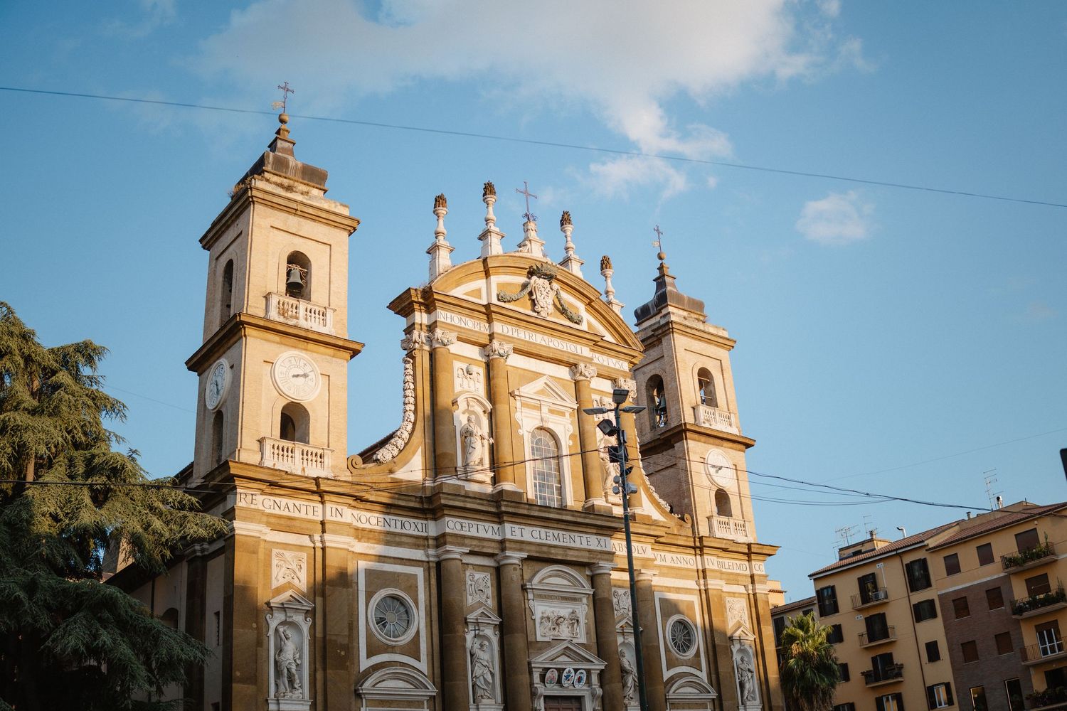 Ornate baroque church facade with golden details and towers against a bright blue sky.