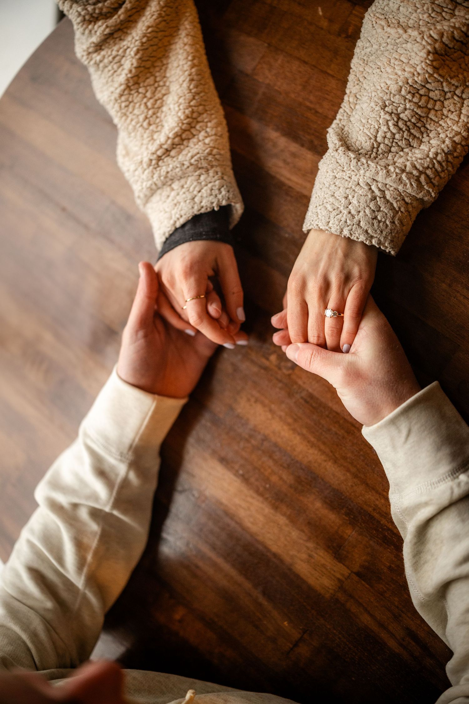 Hands gently touching across a wooden table surface in cozy sweaters.