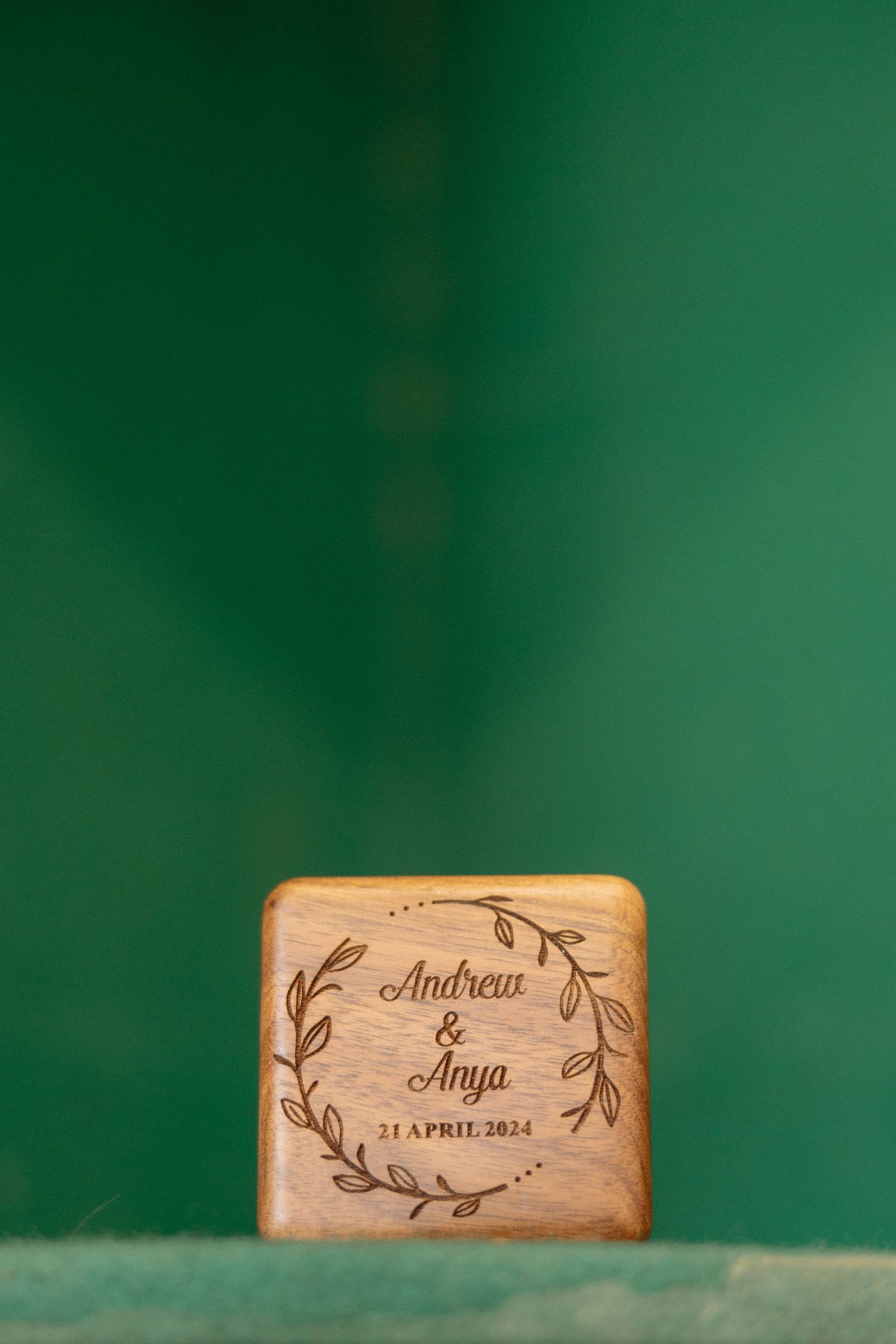 Wooden wine cork with engraved names and floral design on green background.