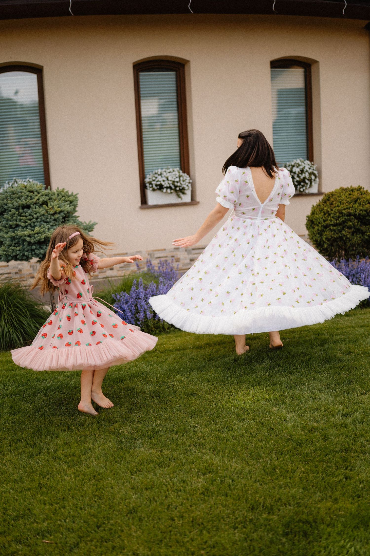 Two floral dresses twirling on a grassy lawn with white and pink tulle skirts in a playful summer scene.