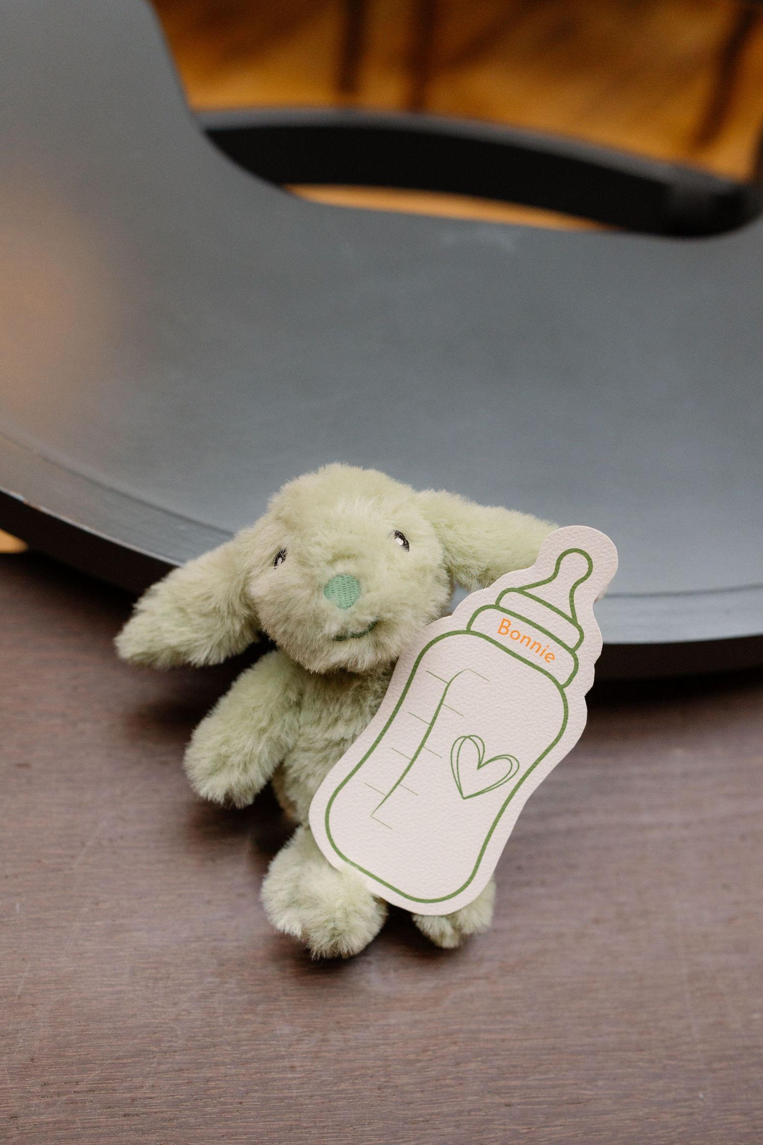 Green plush bunny toy with a baby bottle card on a wooden surface at a celebration event.