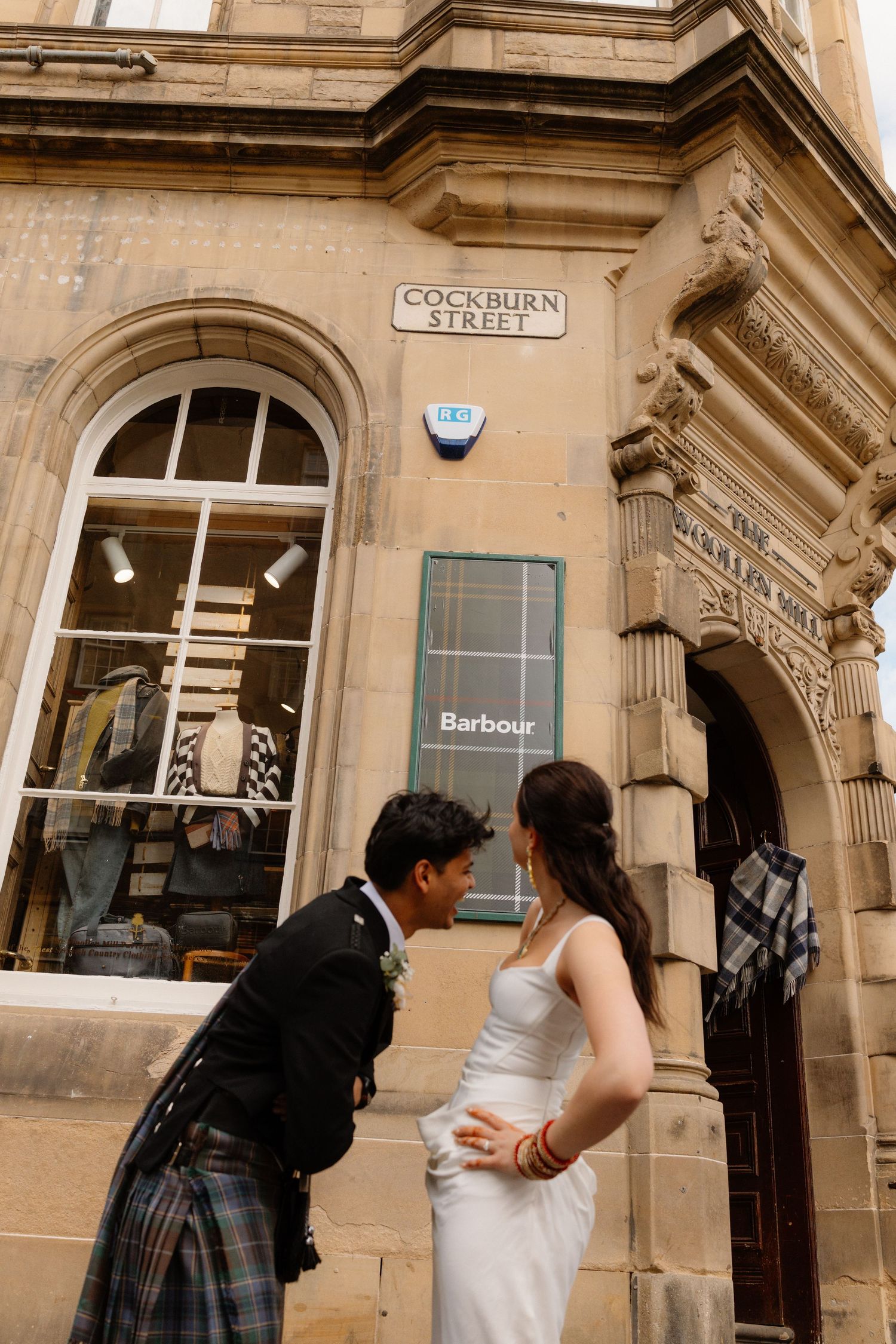Wedding couple sharing an intimate moment outside Barbour store on Cockburn Street Edinburgh in kilt and white dress.