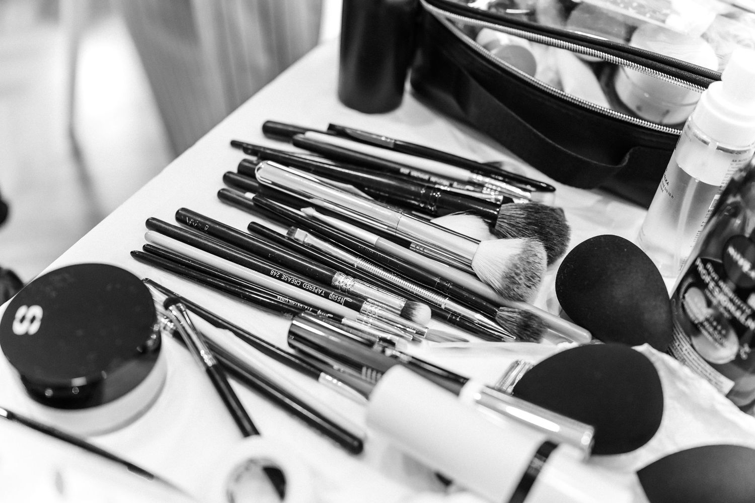 Black and white image of makeup brushes and cosmetic tools arranged on a surface.