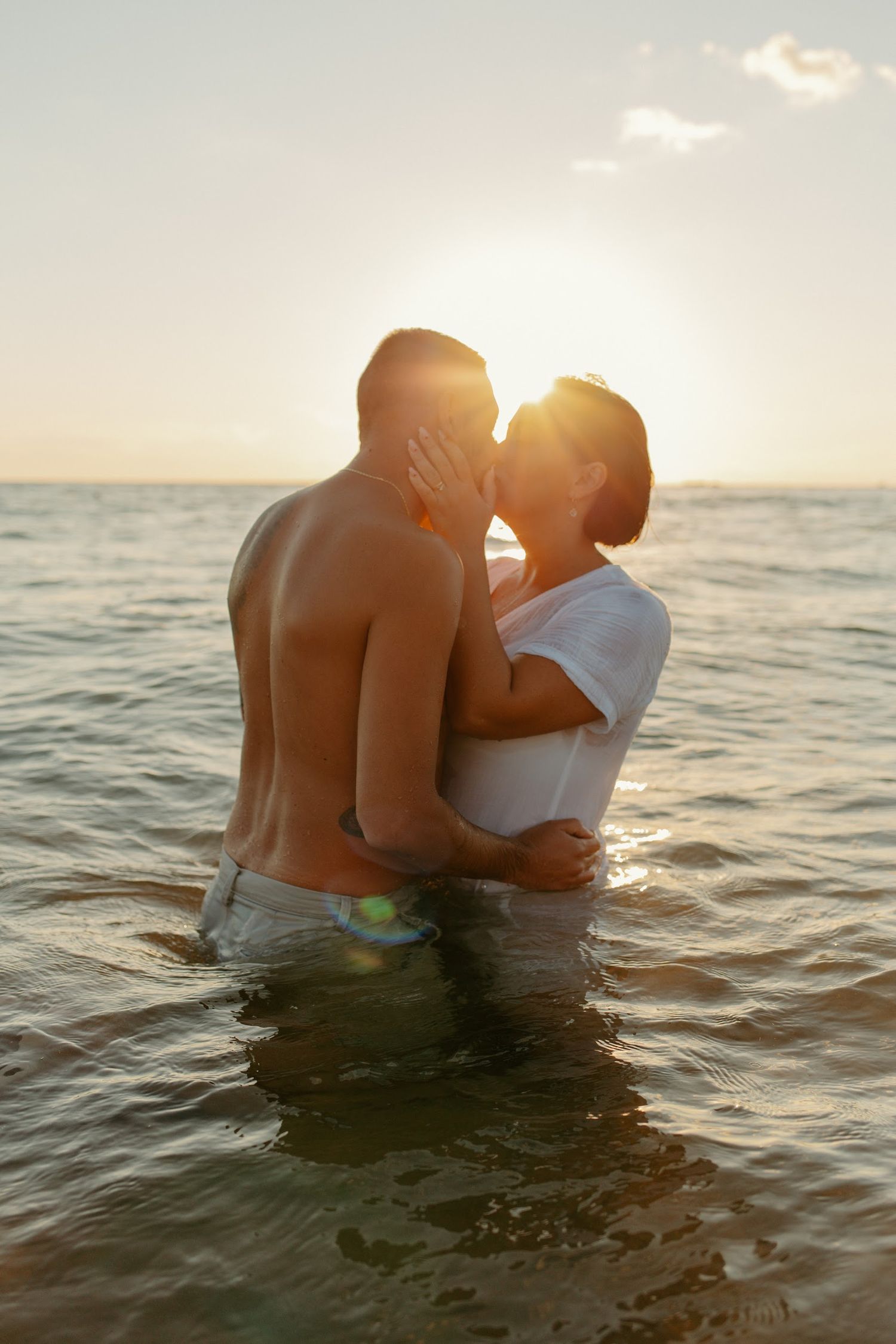 A romantic couple embraces in ocean water during golden hour sunset.