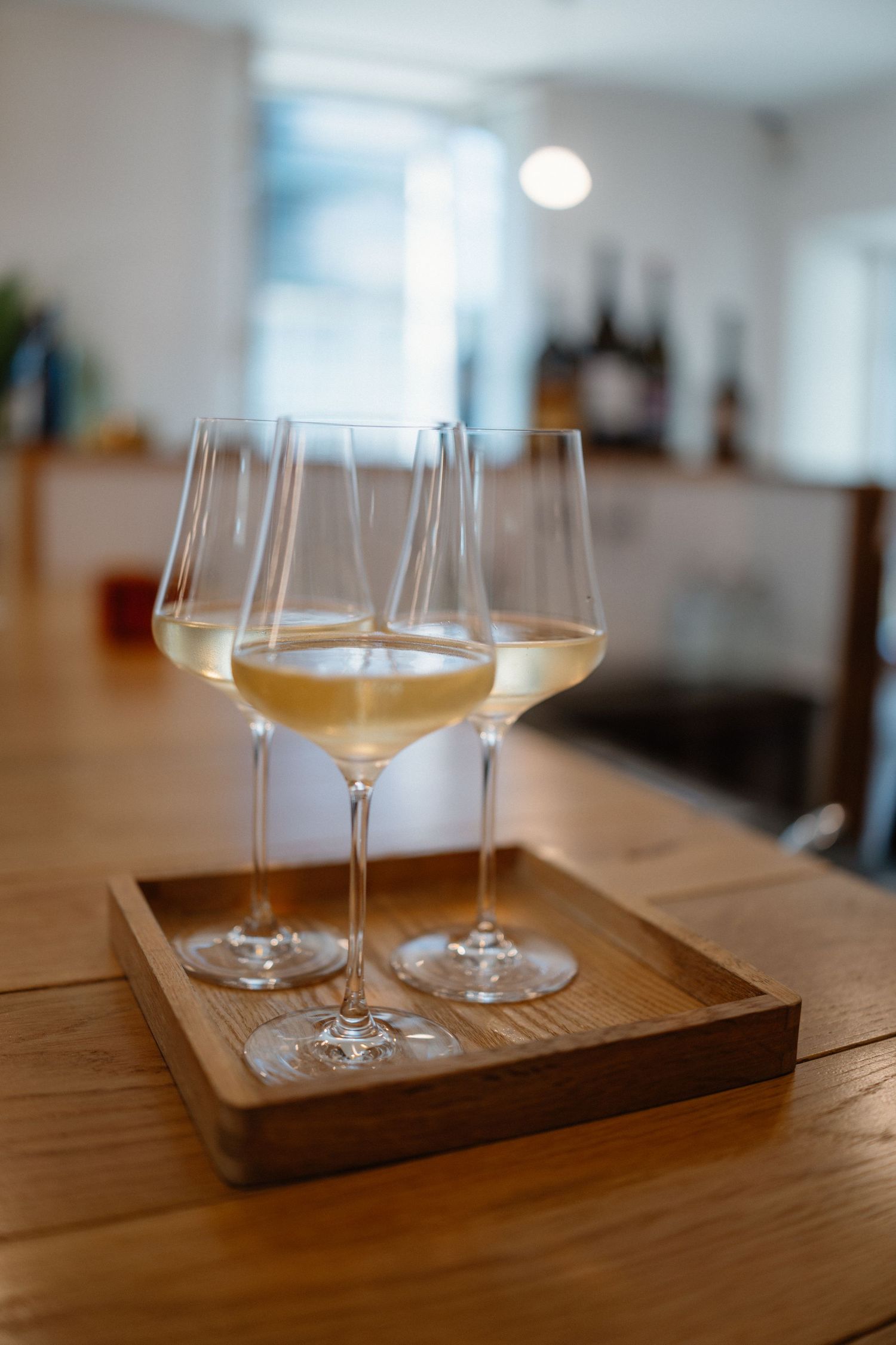 Wine glasses filled with golden liquid arranged on a wooden serving tray.