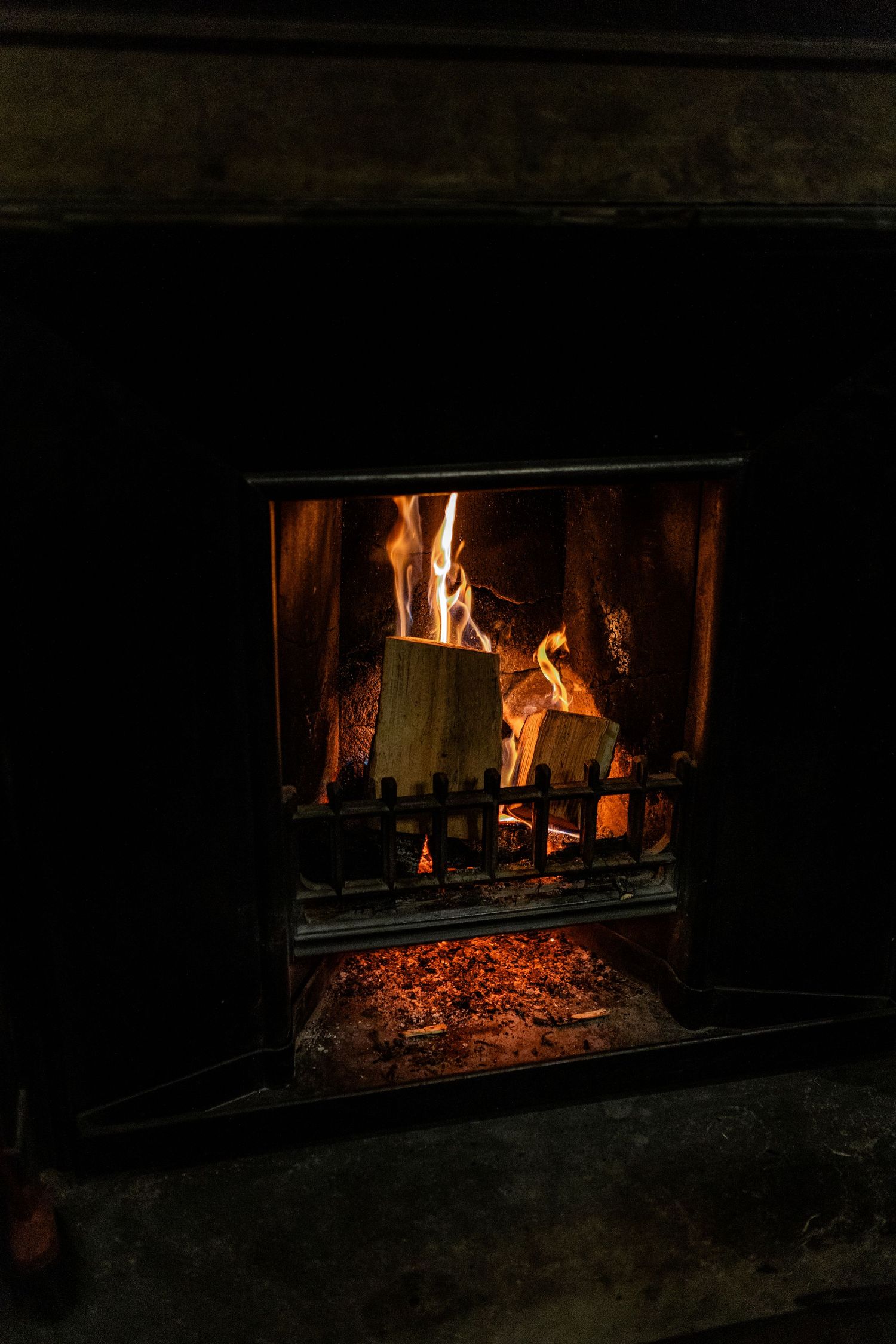 Burning logs and flames in a dark fireplace creating a cozy ambiance.
