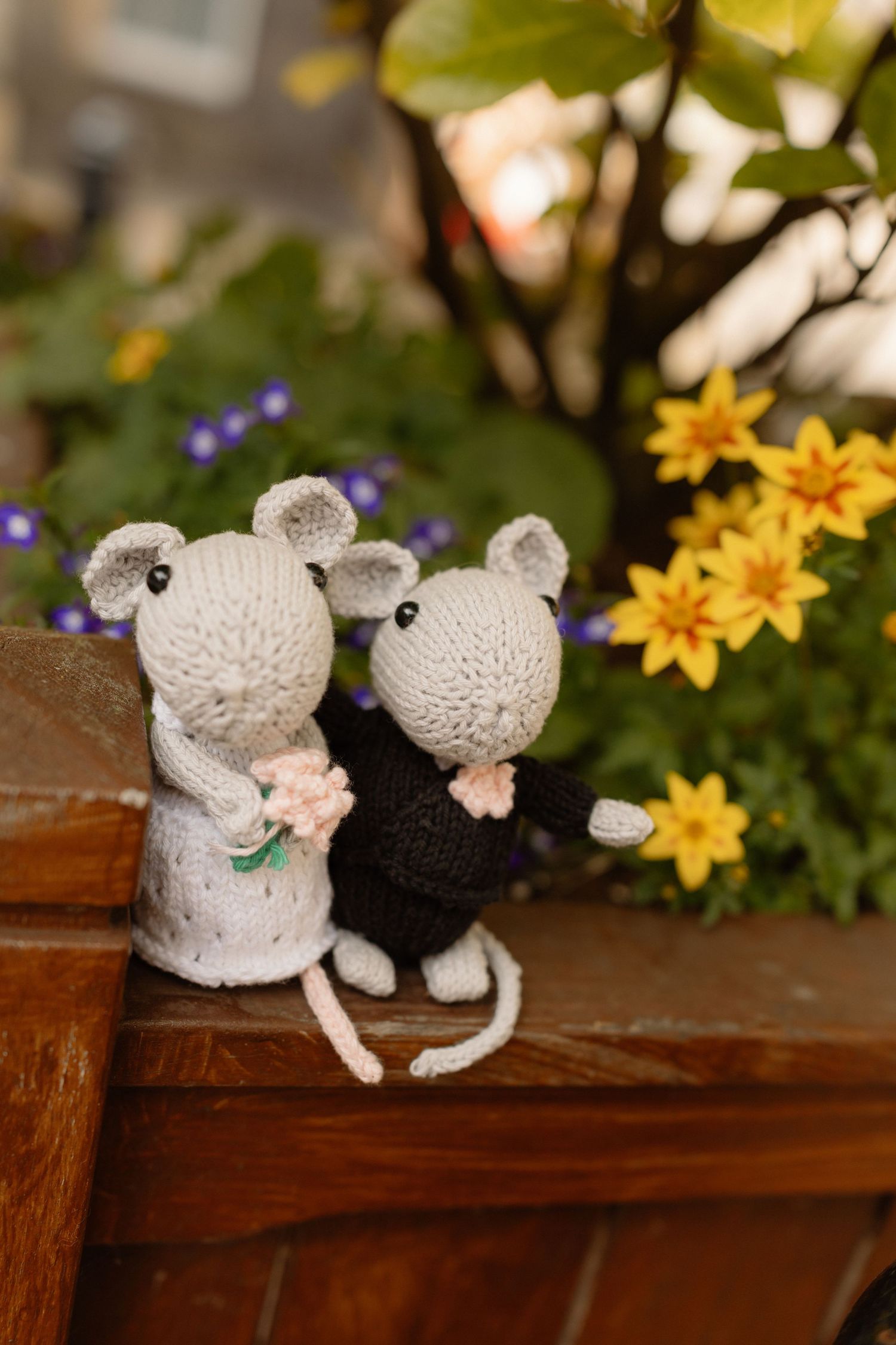 Two knitted mouse wedding couple figurines sitting together with colorful flowers in the background.