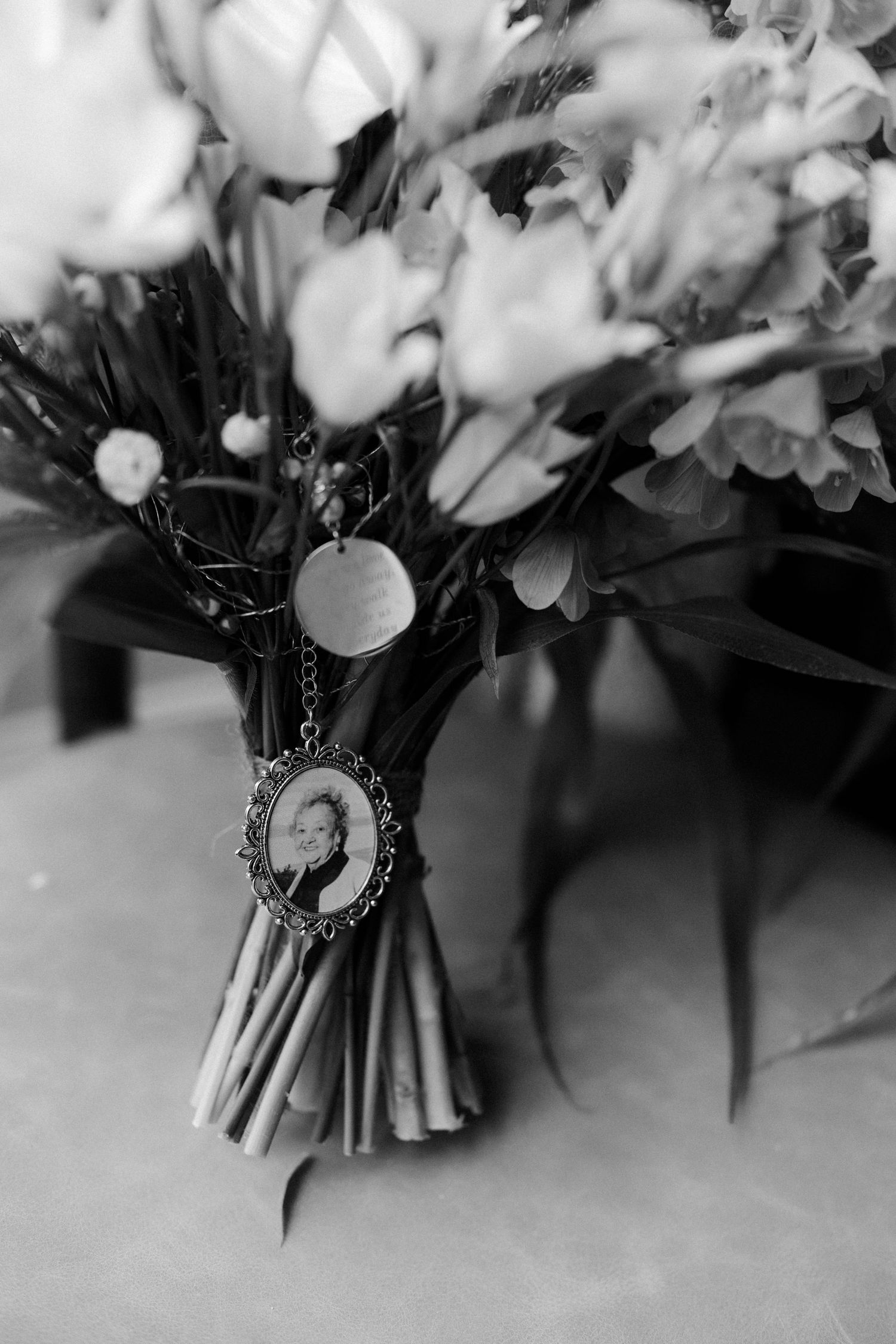 Black and white close-up of a wedding bouquet with a vintage photo memorial charm attached to the stems.