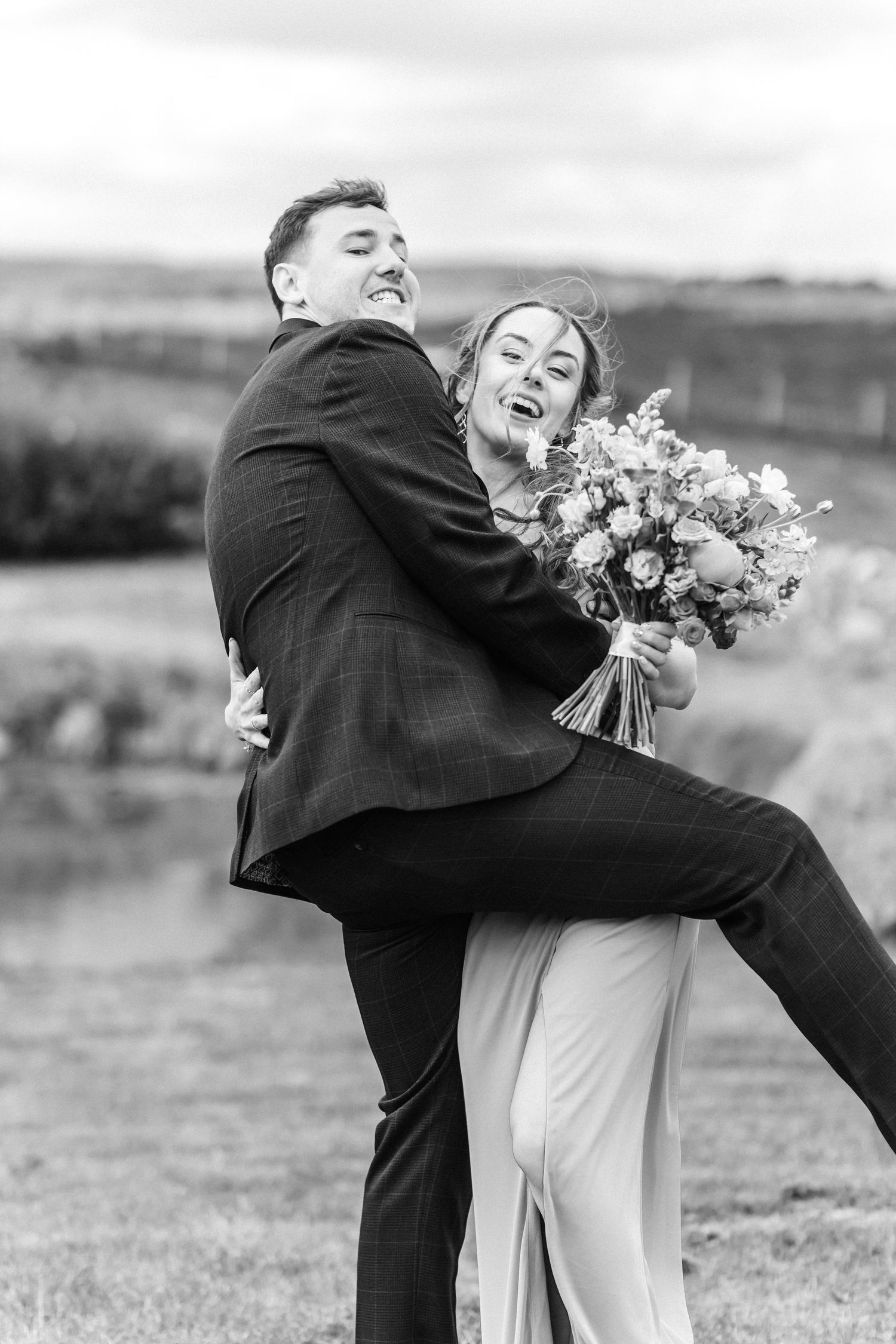 A joyful embrace captured in black and white against a scenic countryside backdrop.