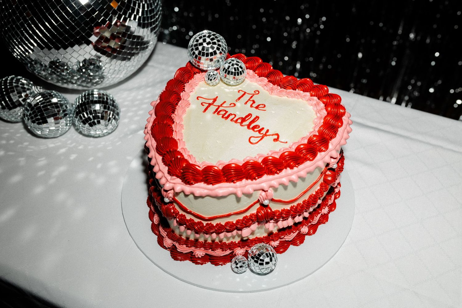 Close-up of a heart-shaped wedding cake with red frosting details on white background.