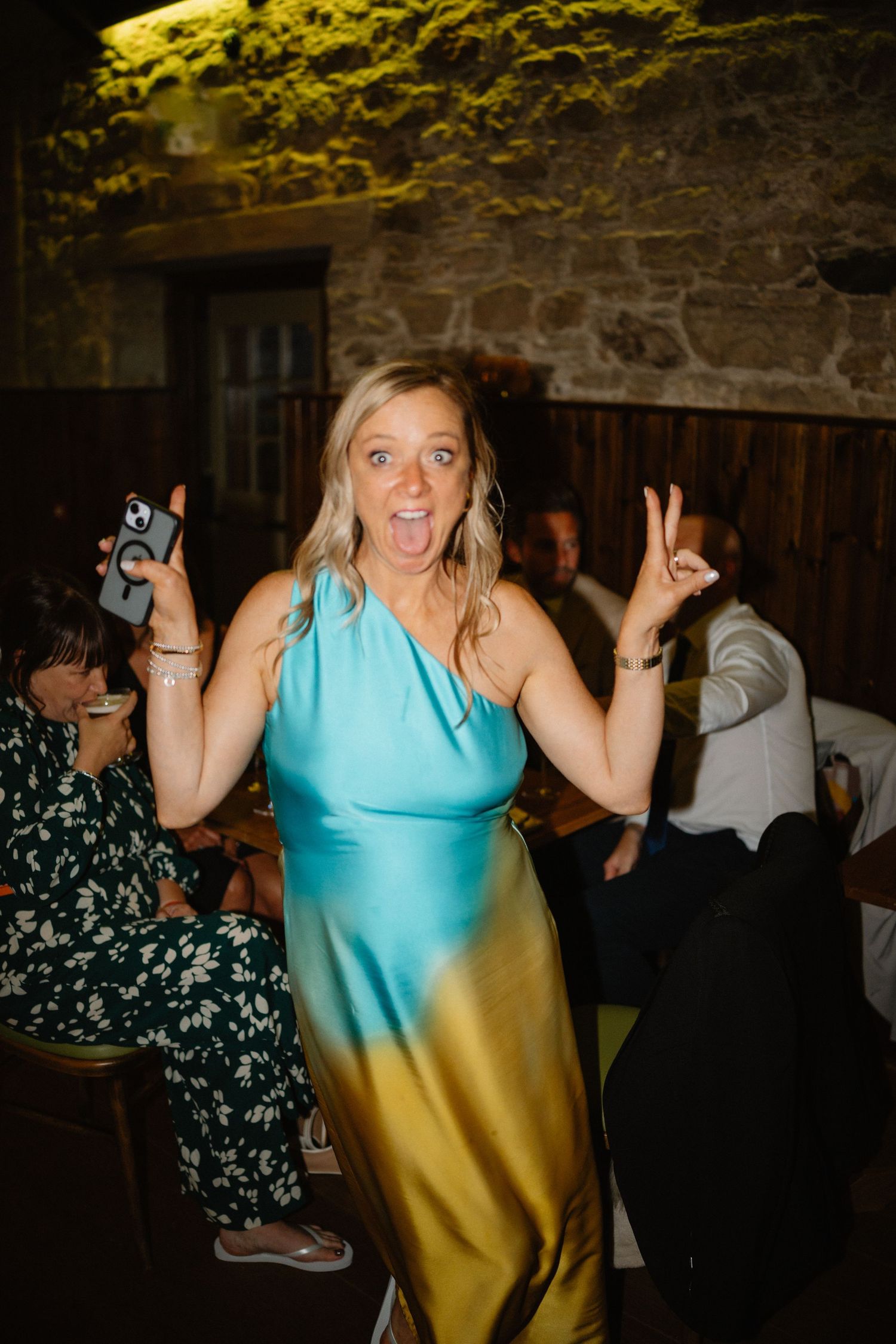 Person in turquoise dress dancing enthusiastically at an indoor party venue.