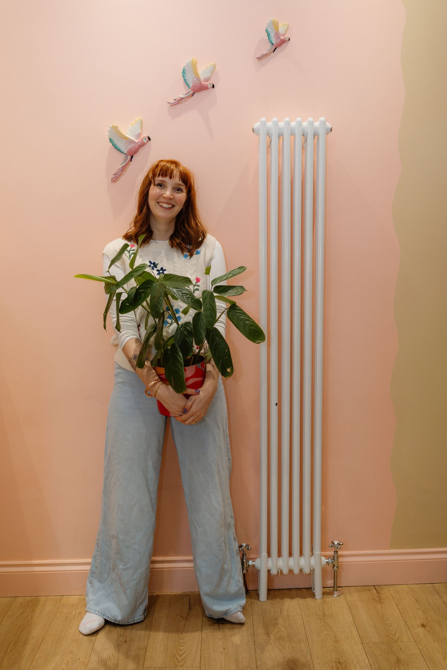 Standing against a pink wall with white radiator holding fresh flowers.