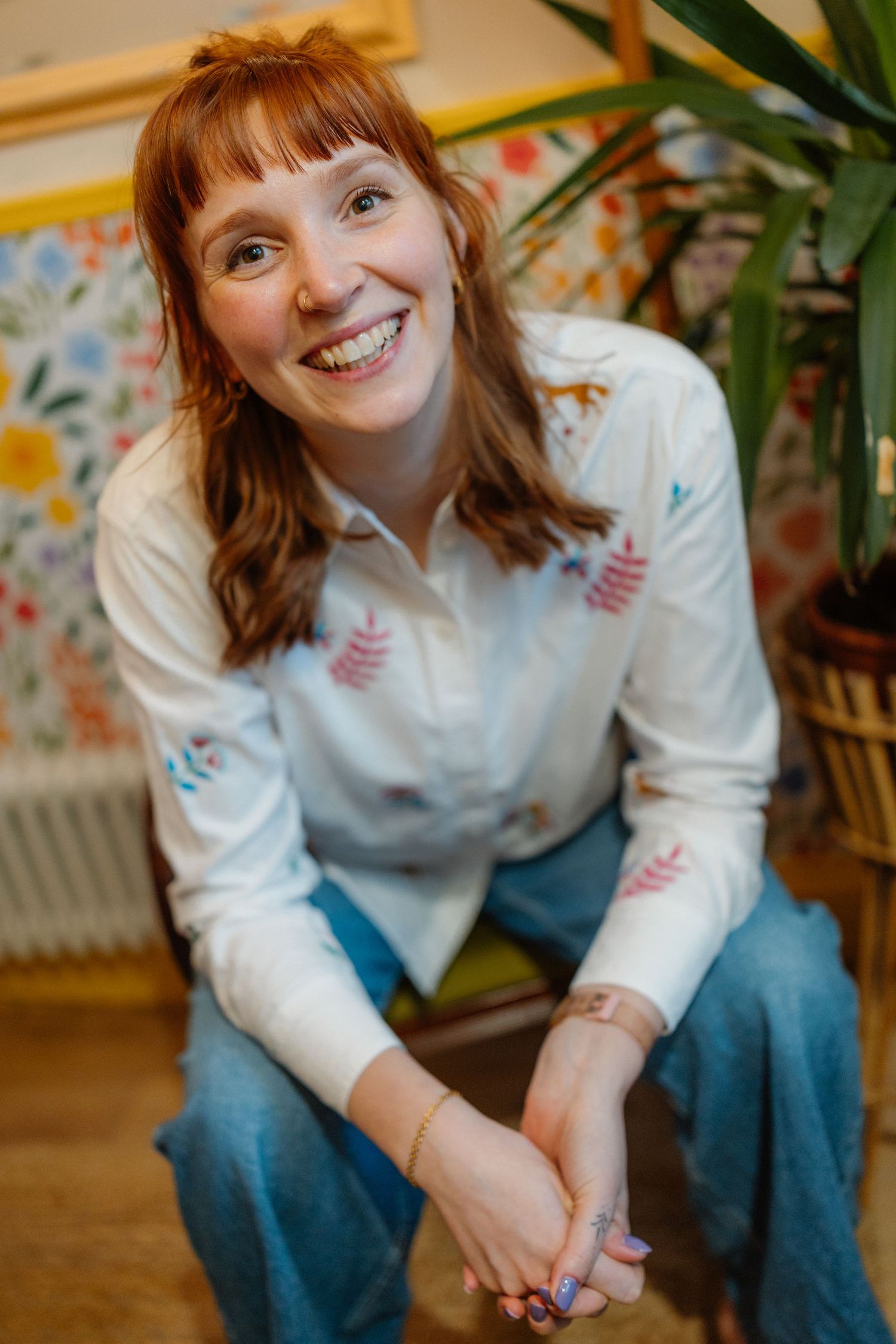 Person in white sweater sitting casually by indoor plants.