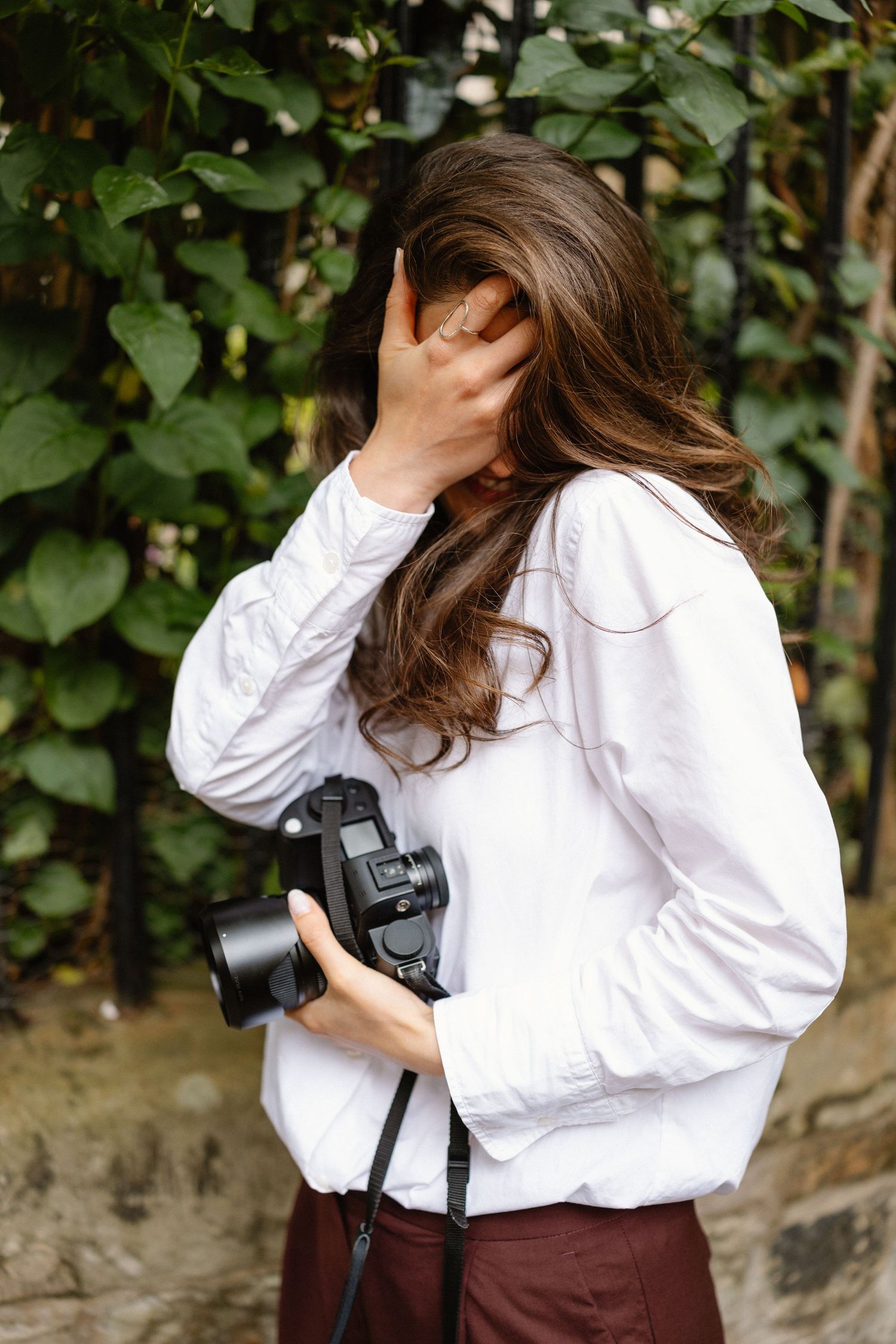 Photographer in white shirt holding camera while covering face with hand.