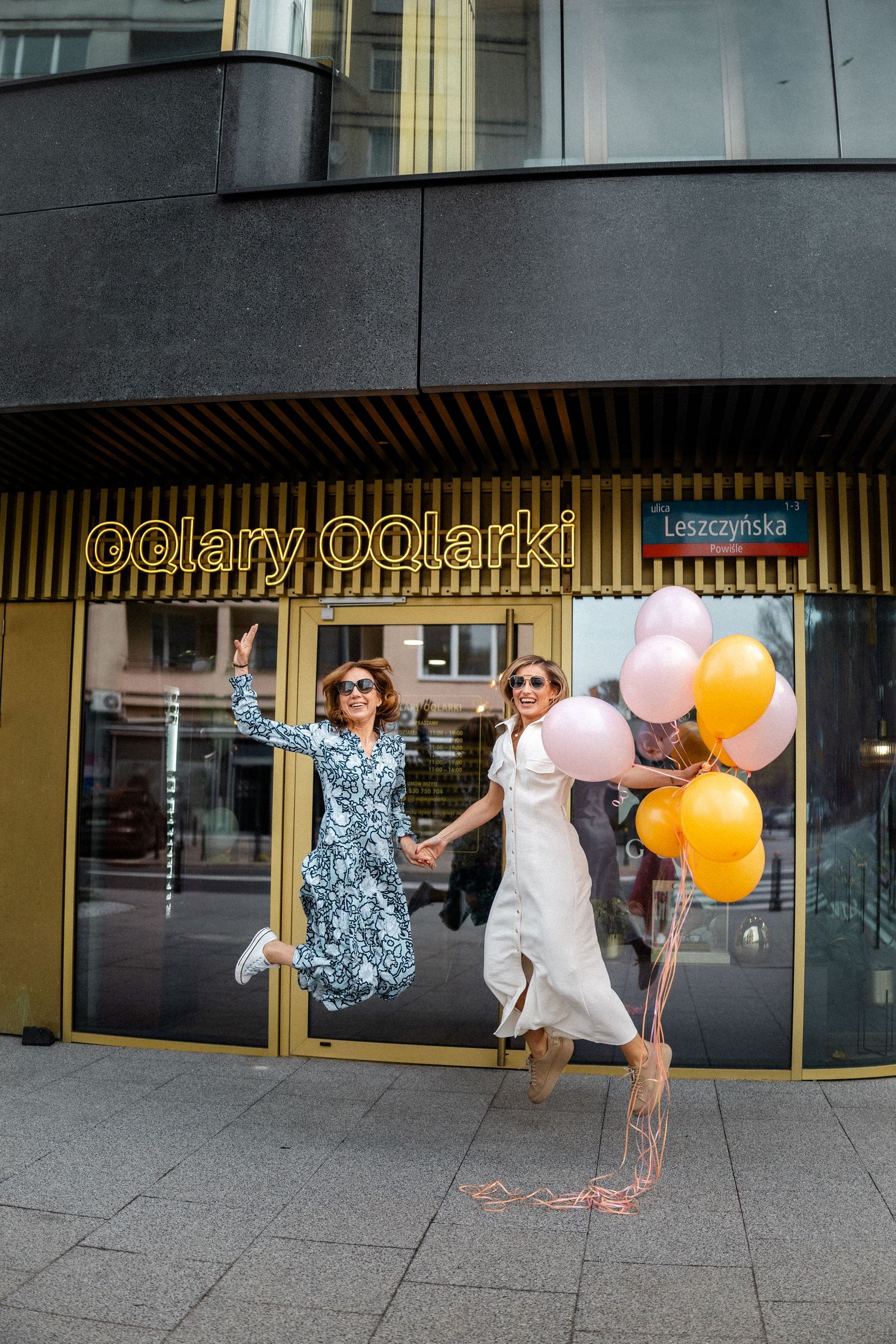 Two people jumping joyfully outside optical store with balloons.