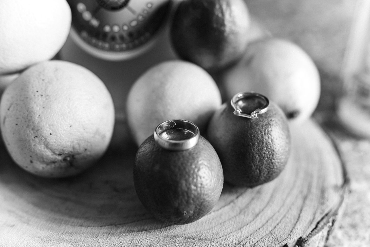 Black and white photo of two wedding rings resting on small round fruits arranged on a wooden board.
