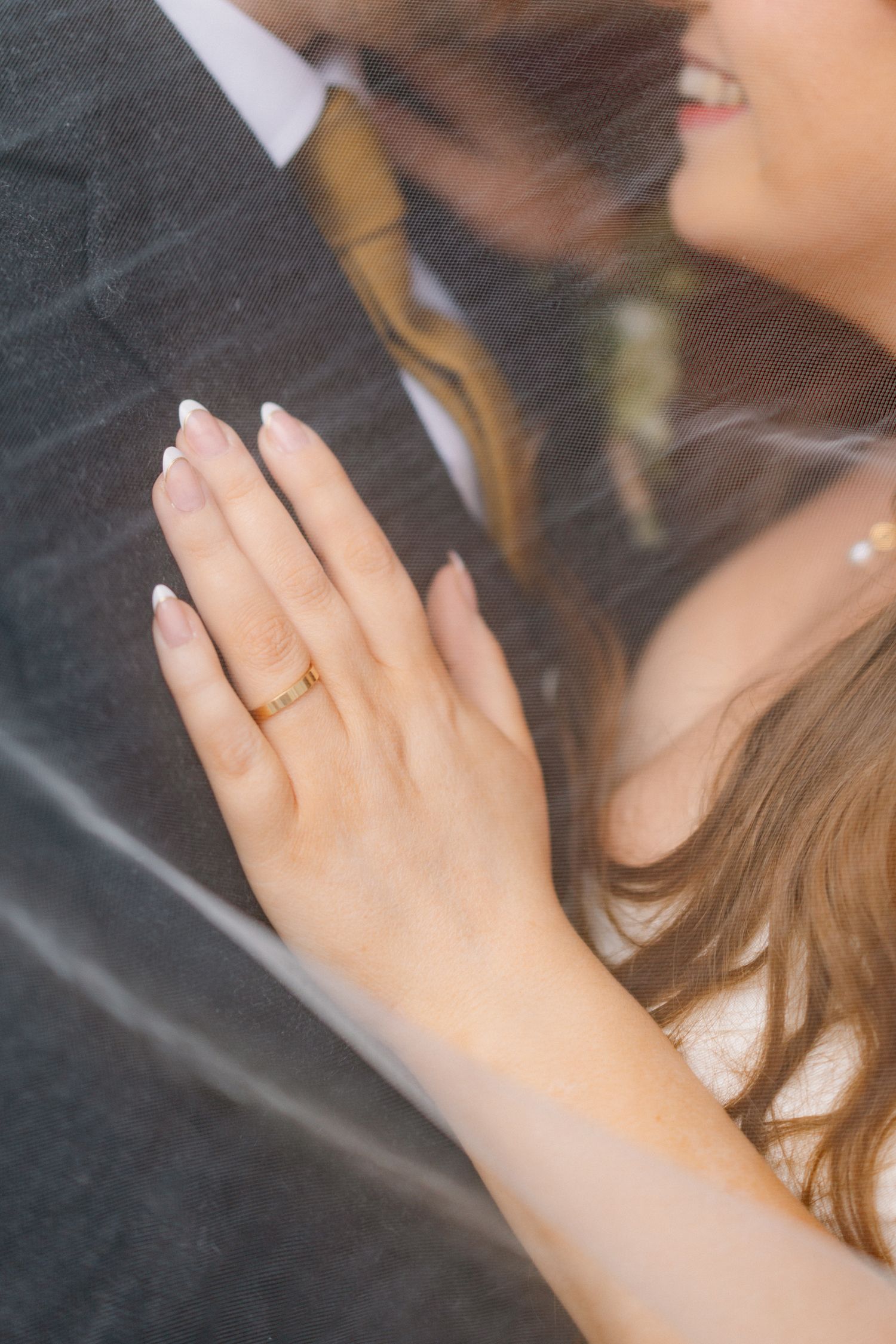 Close-up of a bride smiling with her hand resting on the groom showing a delicate gold wedding band.