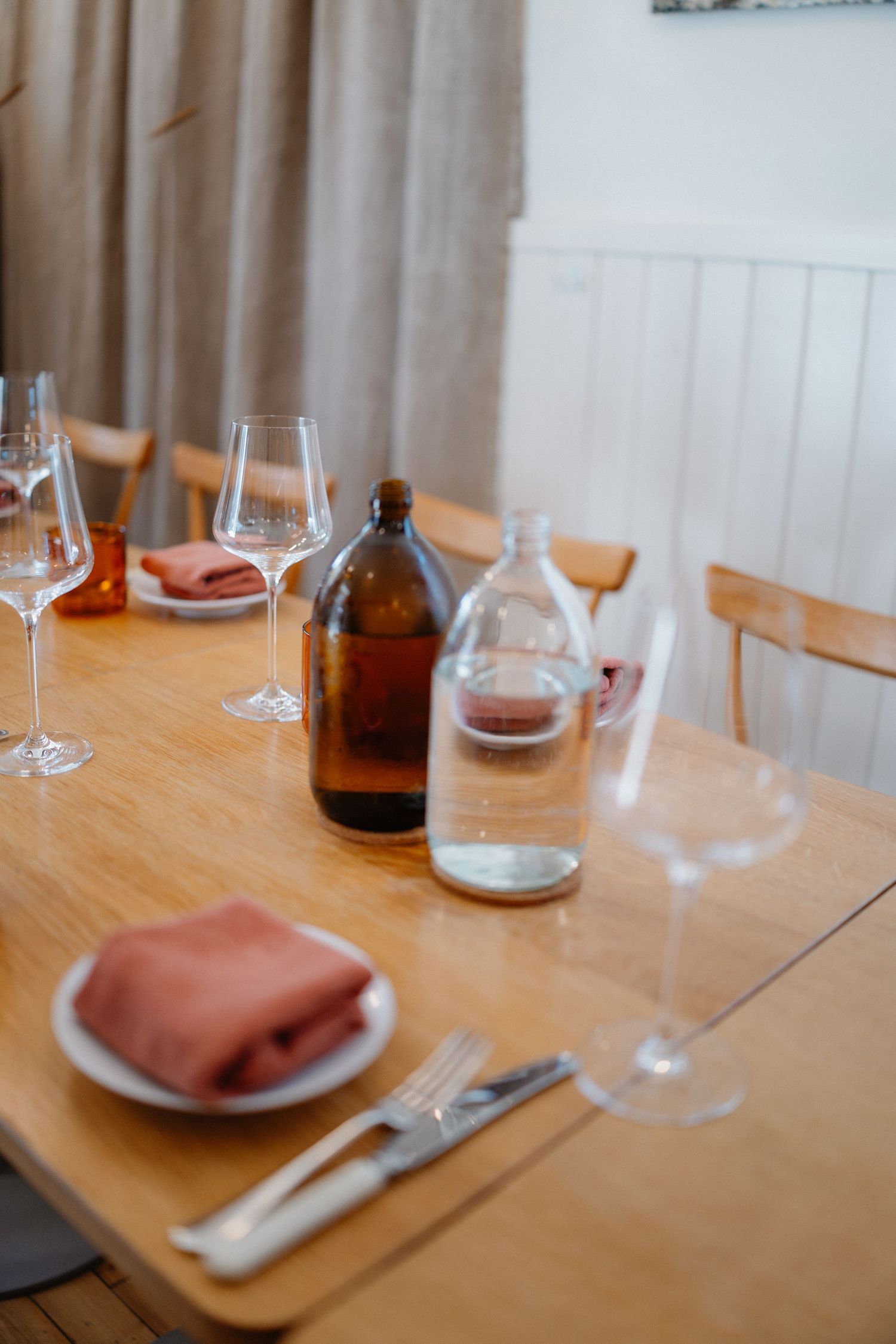 Elegant wooden dining table set with wine glasses, terracotta napkins, and glass bottles.