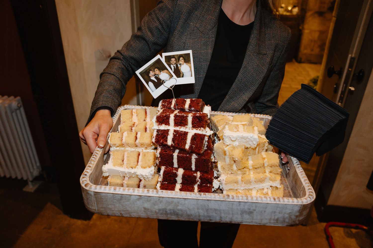 Person holds tray of assorted mini sandwiches with Polaroid photos at wedding catering event.