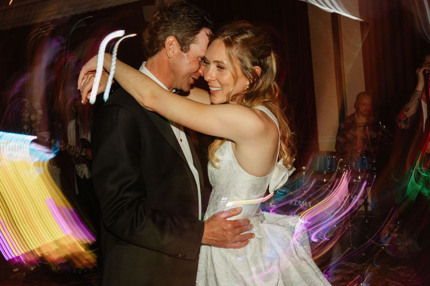 Bride and groom sharing romantic first dance surrounded by colorful light trails at reception.