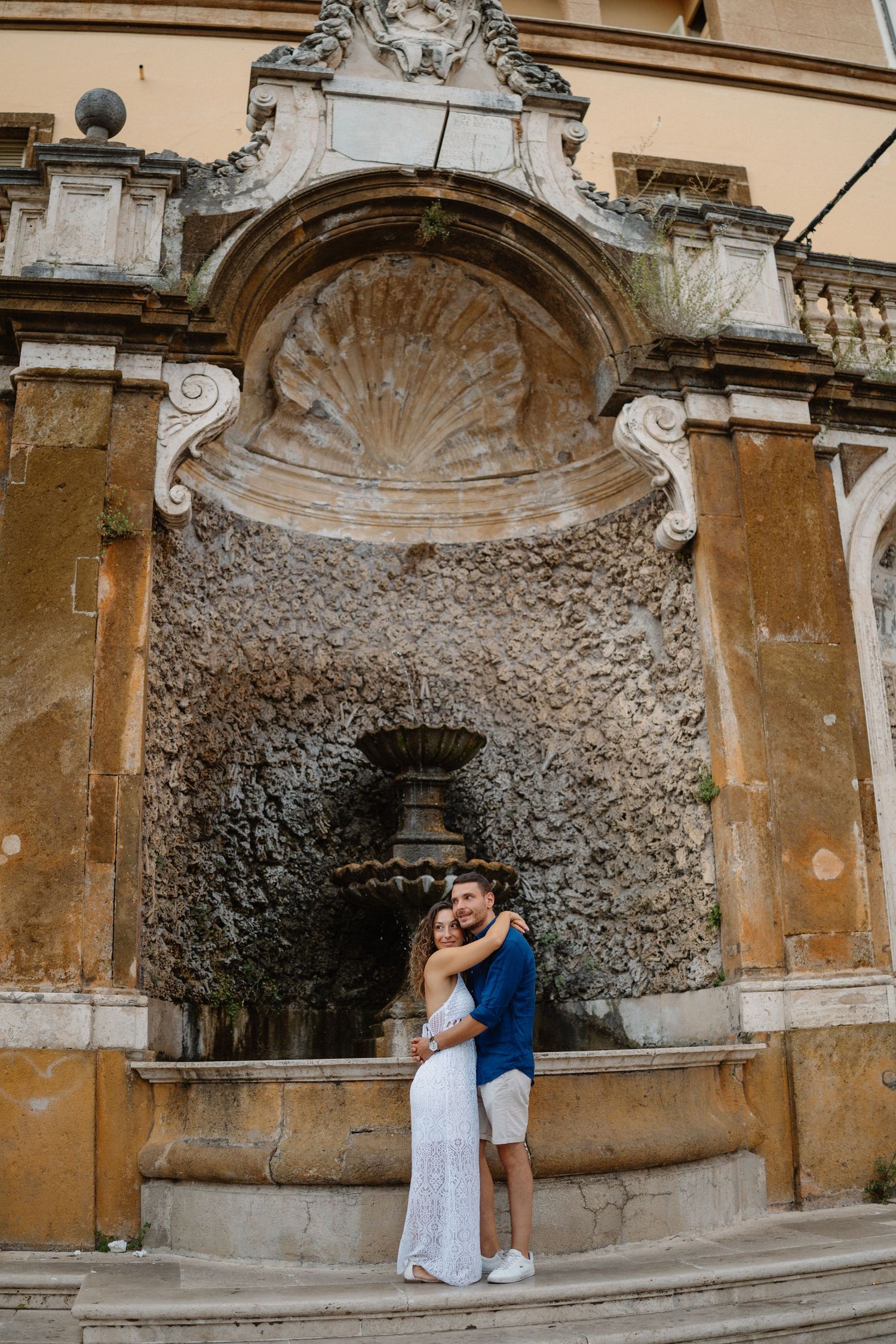 Romantic couple posing against ornate stone grotto wall with decorative arches.