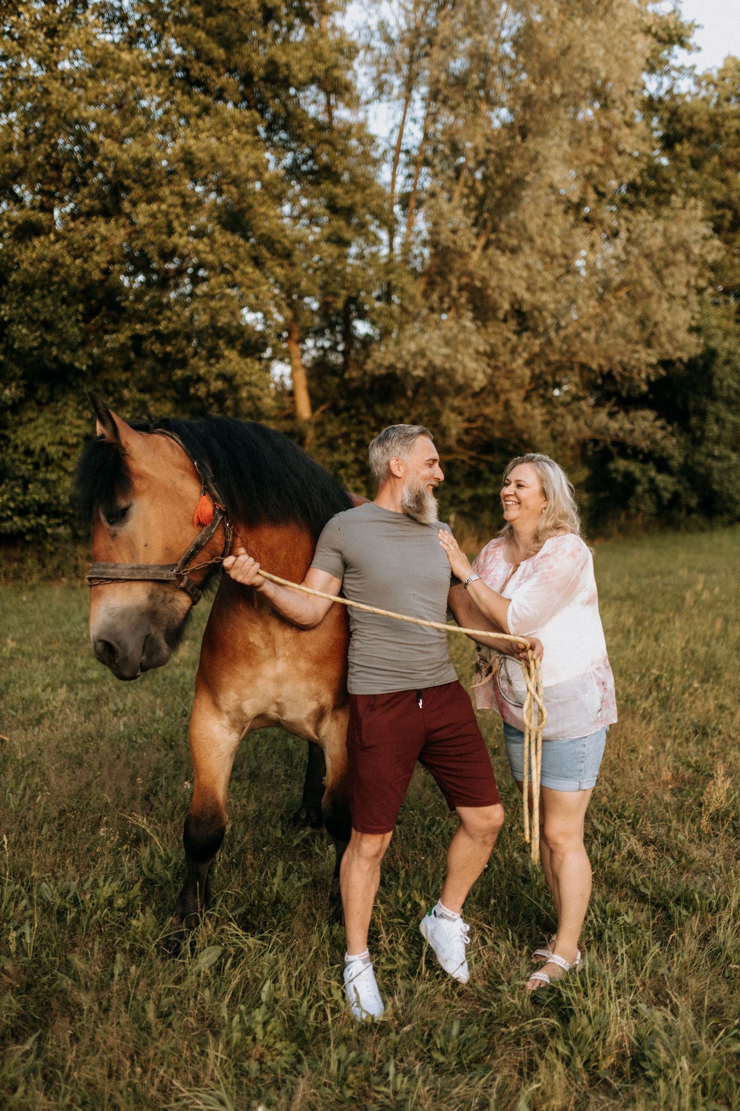 A couple poses playfully with their horse in a sunlit autumn field.