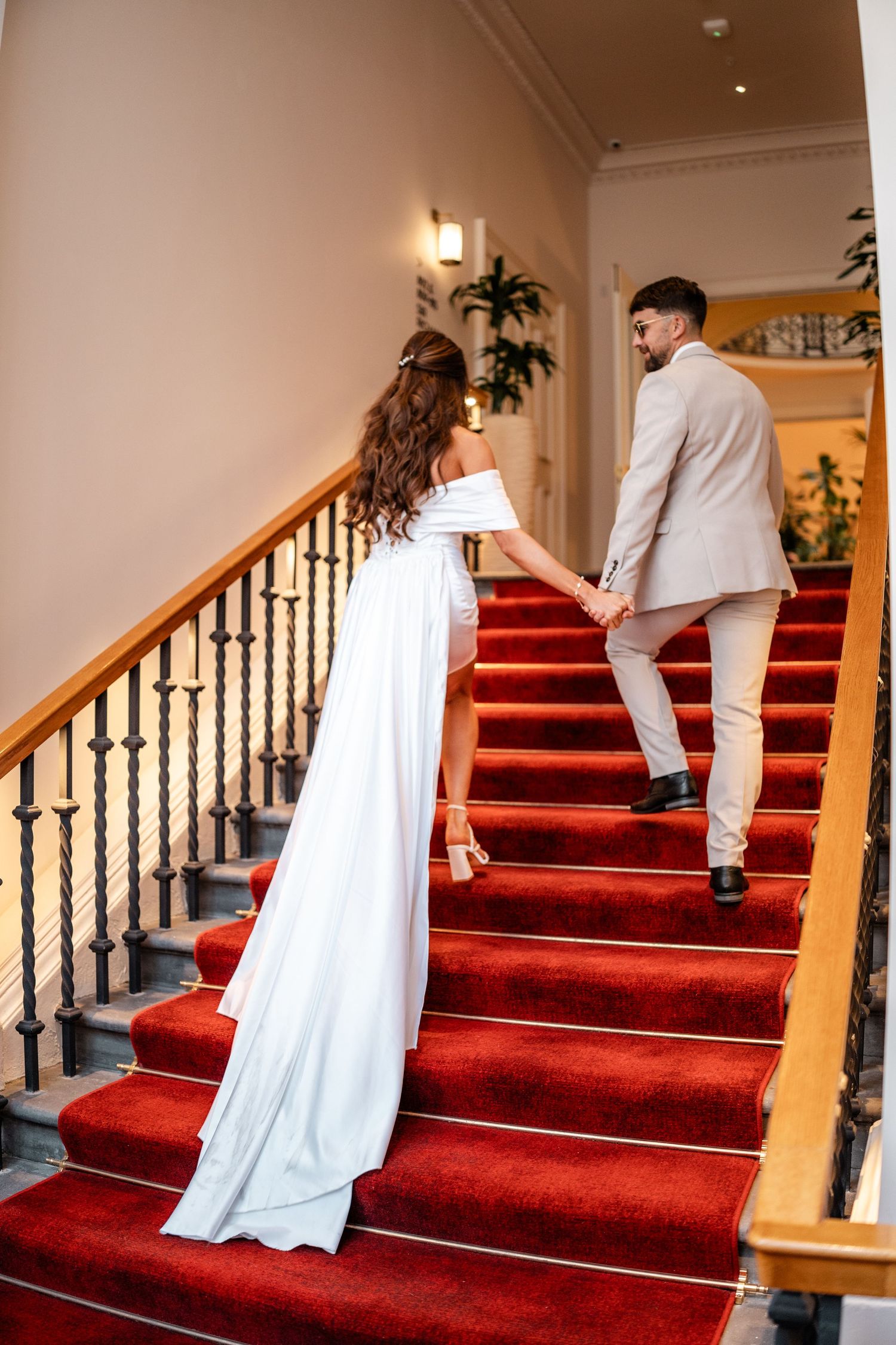 Couple ascending elegant red-carpeted stairs with ornate black railings.