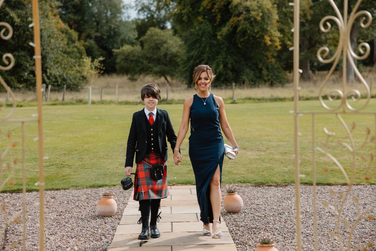 Children in formal attire walking through decorative garden arches at outdoor wedding venue.
