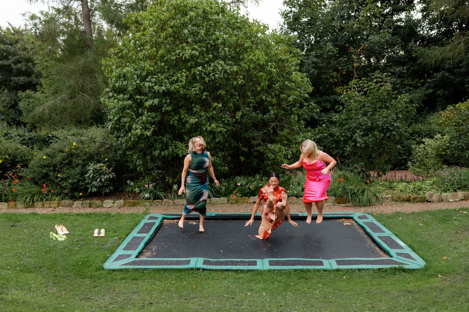 People enjoying outdoor activities on a large trampoline in a lush green garden setting.