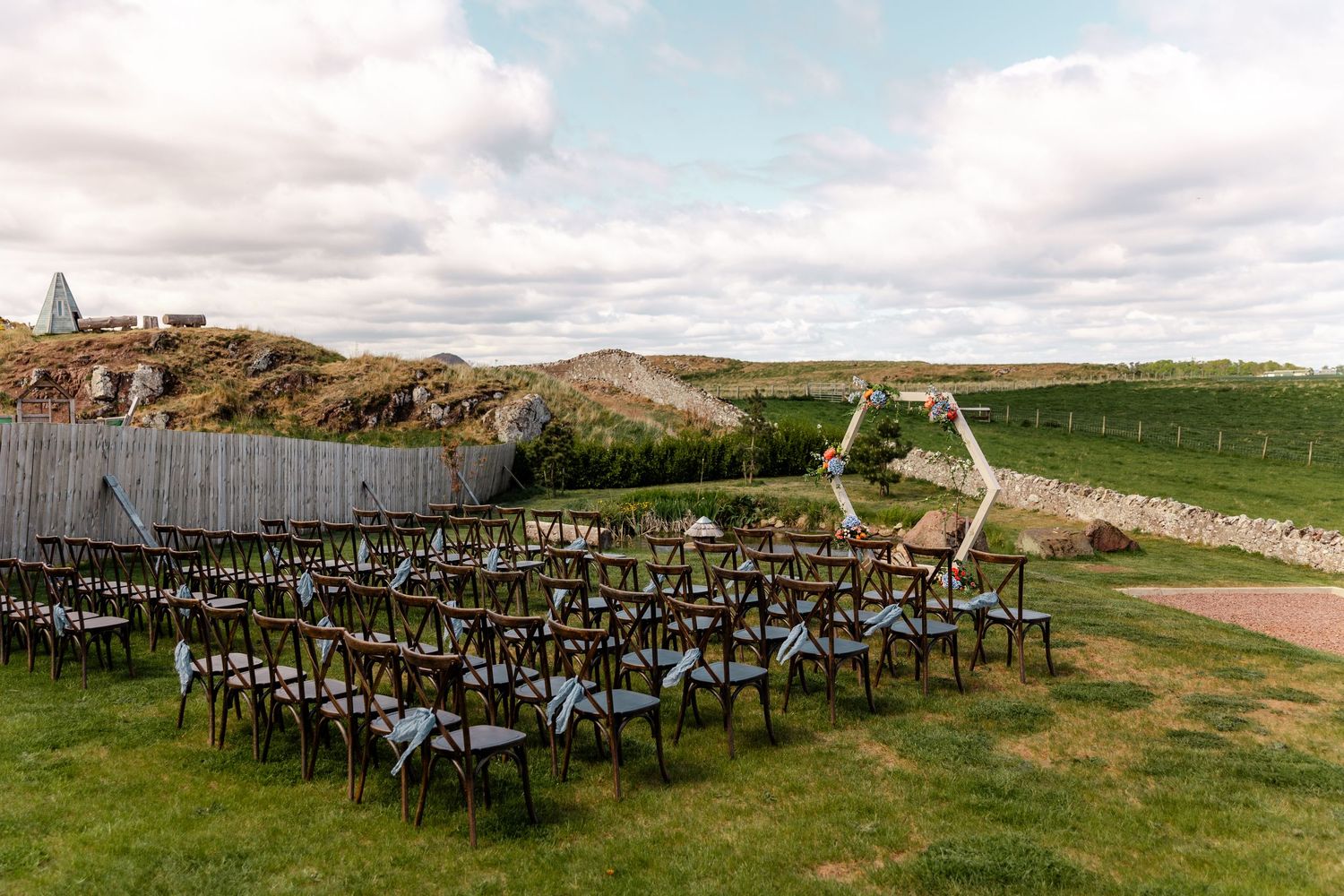 Outdoor wedding ceremony setup with rows of dark chairs and mountain landscape backdrop.