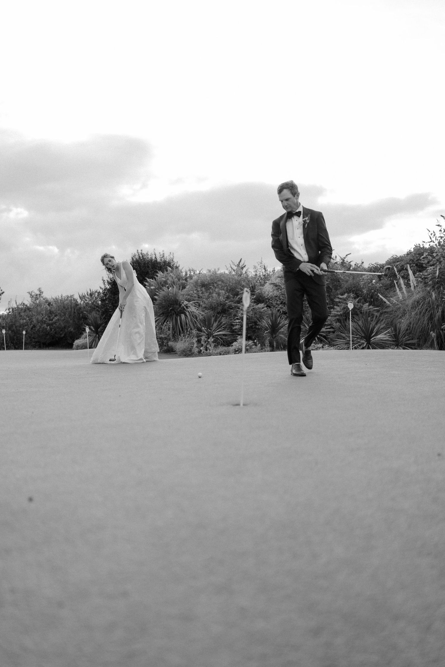 Black and white photo of bride and groom playing golf on wedding day.